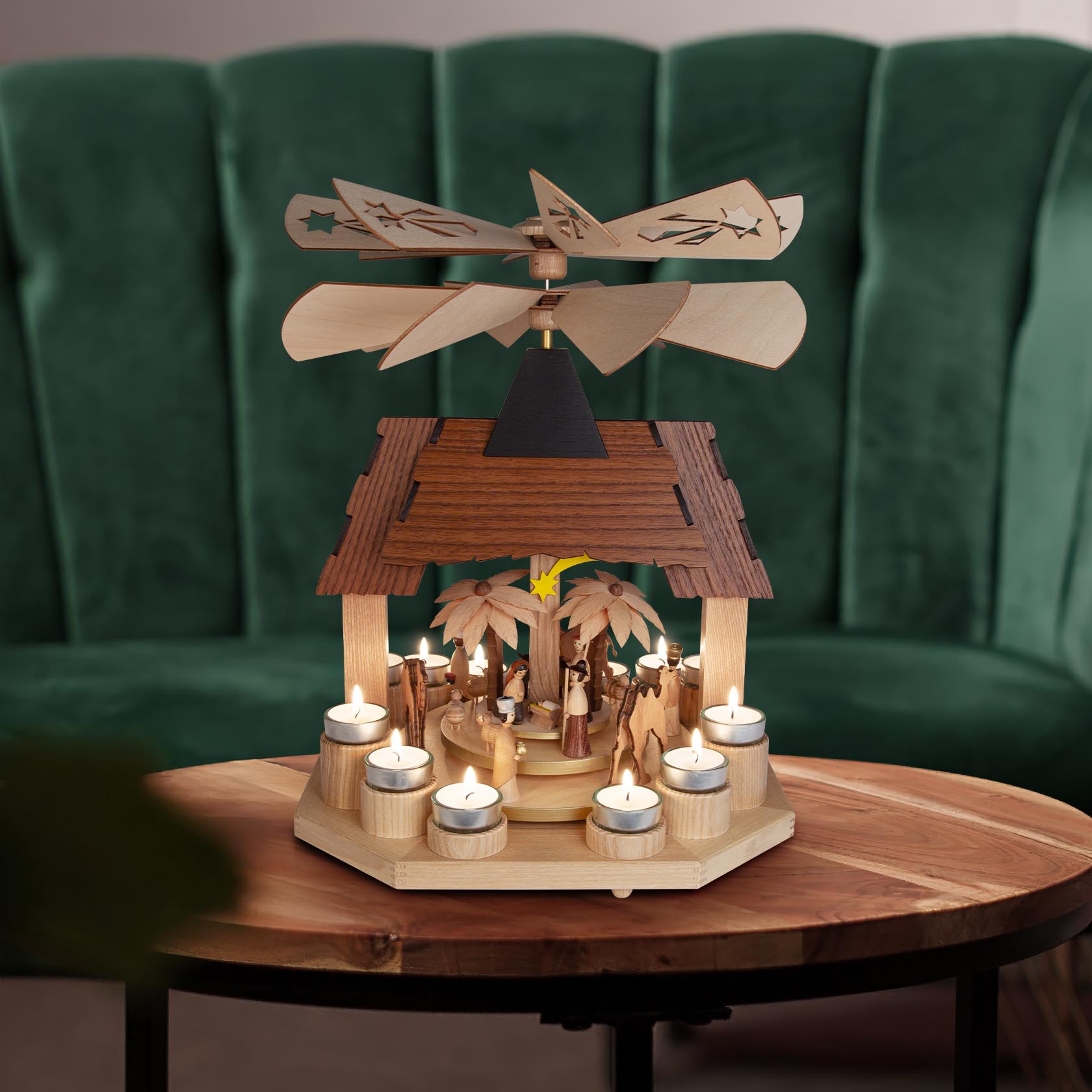 A wooden Christmas pyramid featuring a nativity scene with figures, two rotating wing wheels, and lit with tealight candles on a wooden table.