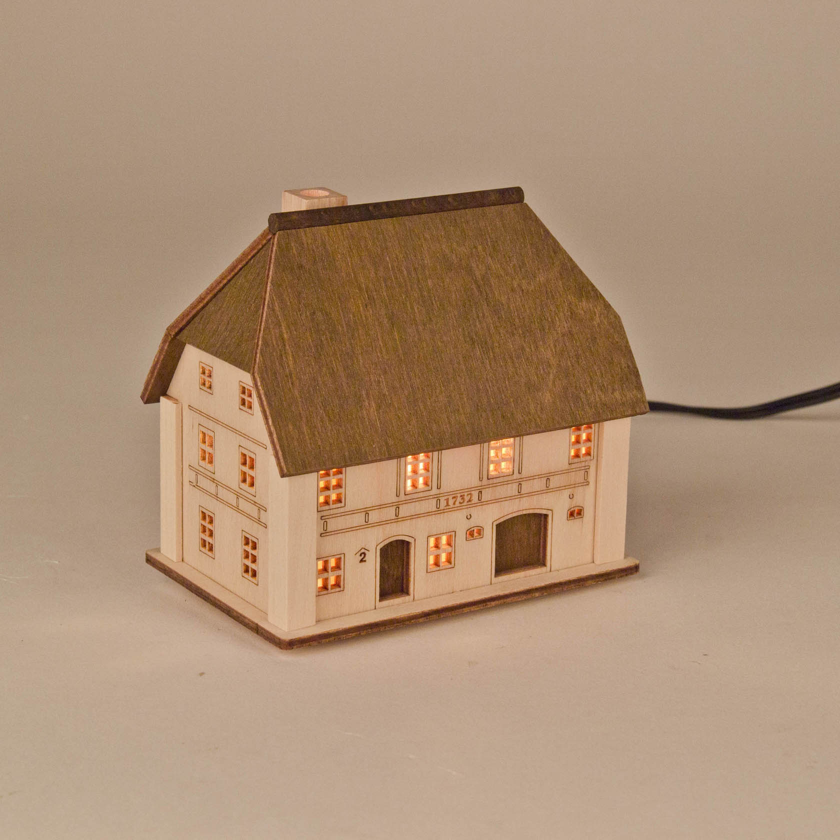 A wooden light-up miniature model of a farmhouse with lit windows and a thatched roof.