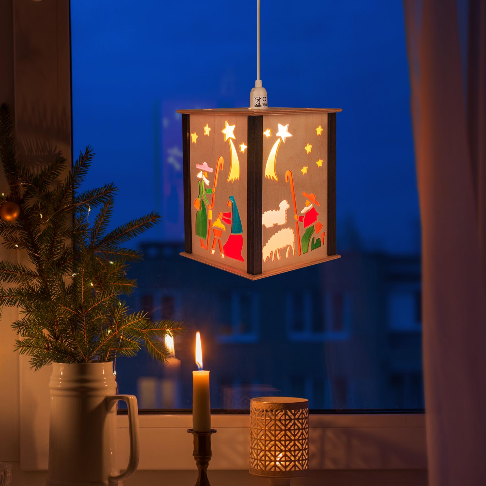 A decorative hanging lantern depicting the Nativity scene with Mary, Joseph, baby Jesus, and shepherds under stars, illuminated by a warm light.