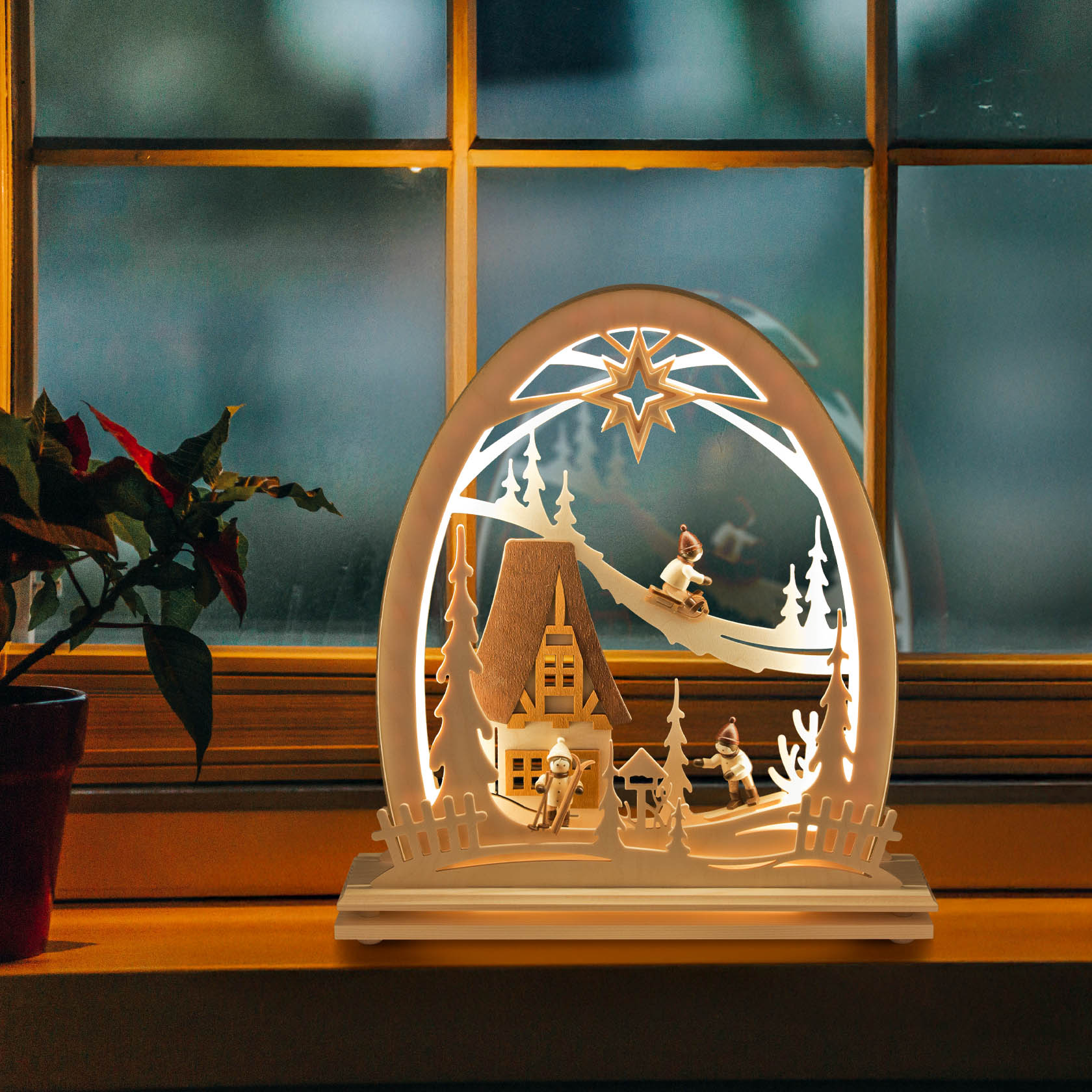 Ein Erzgebirgsbogen mit LED-Beleuchtung zeigt zwei Kinder beim Rodeln im Schnee, ein Haus und einen Weihnachtsstern.