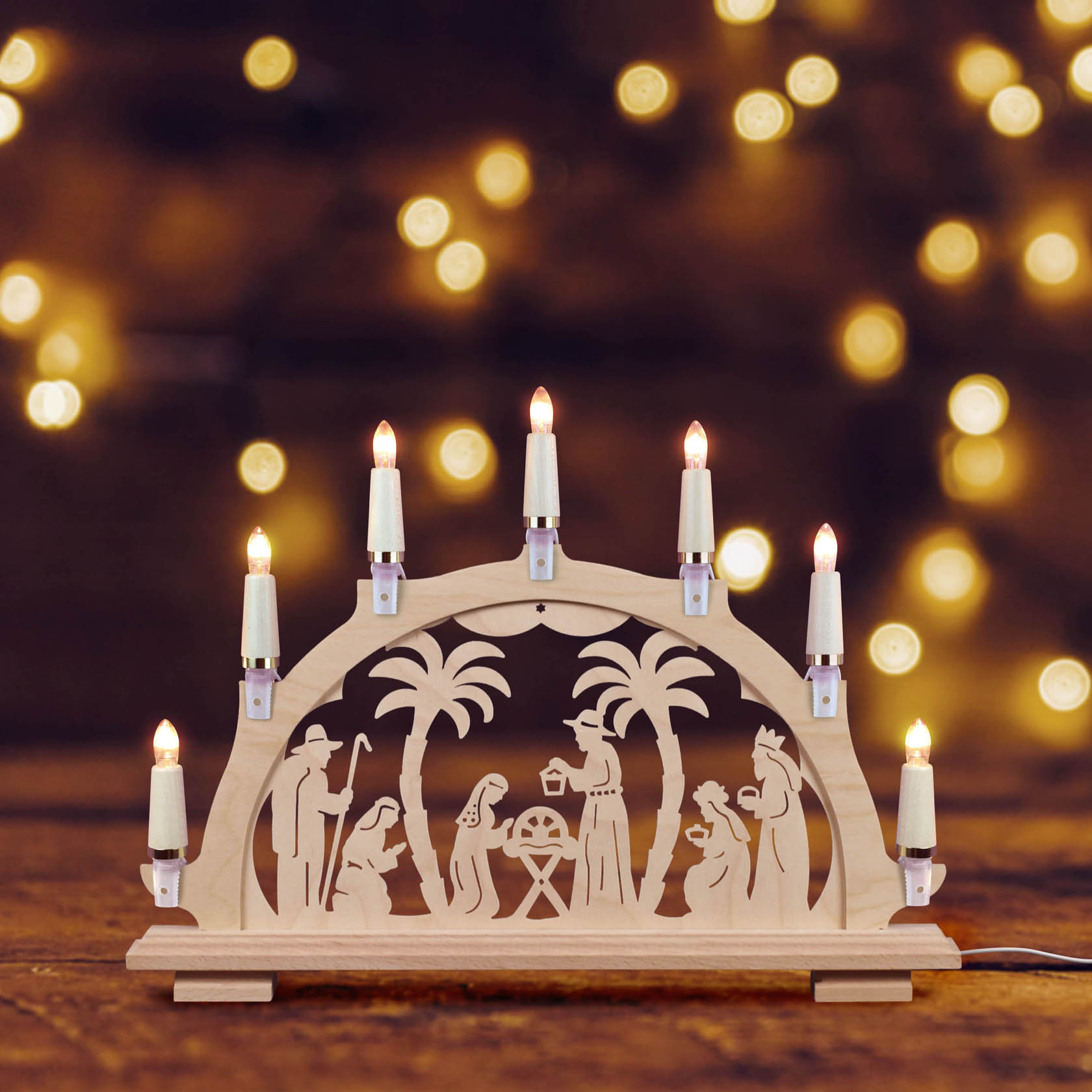 A 7-piece candle arch with wooden maple frame, depicting a nativity scene with figures under a palm tree and glowing lights on top.