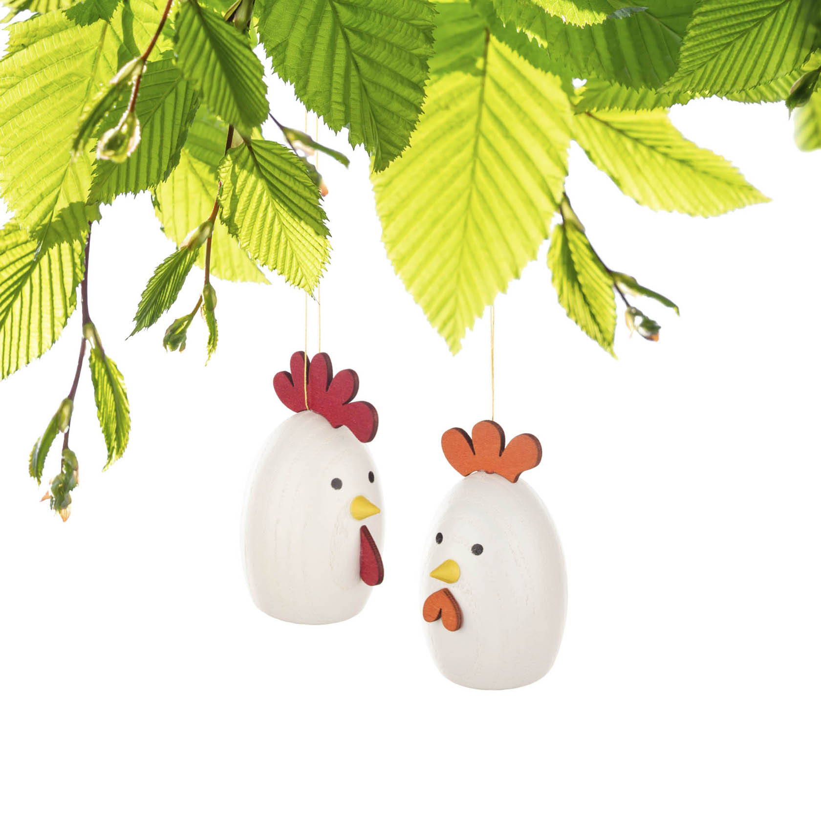 Two hanging decorative wooden ornaments shaped like a rooster and a hen with red combs, under green leaves.