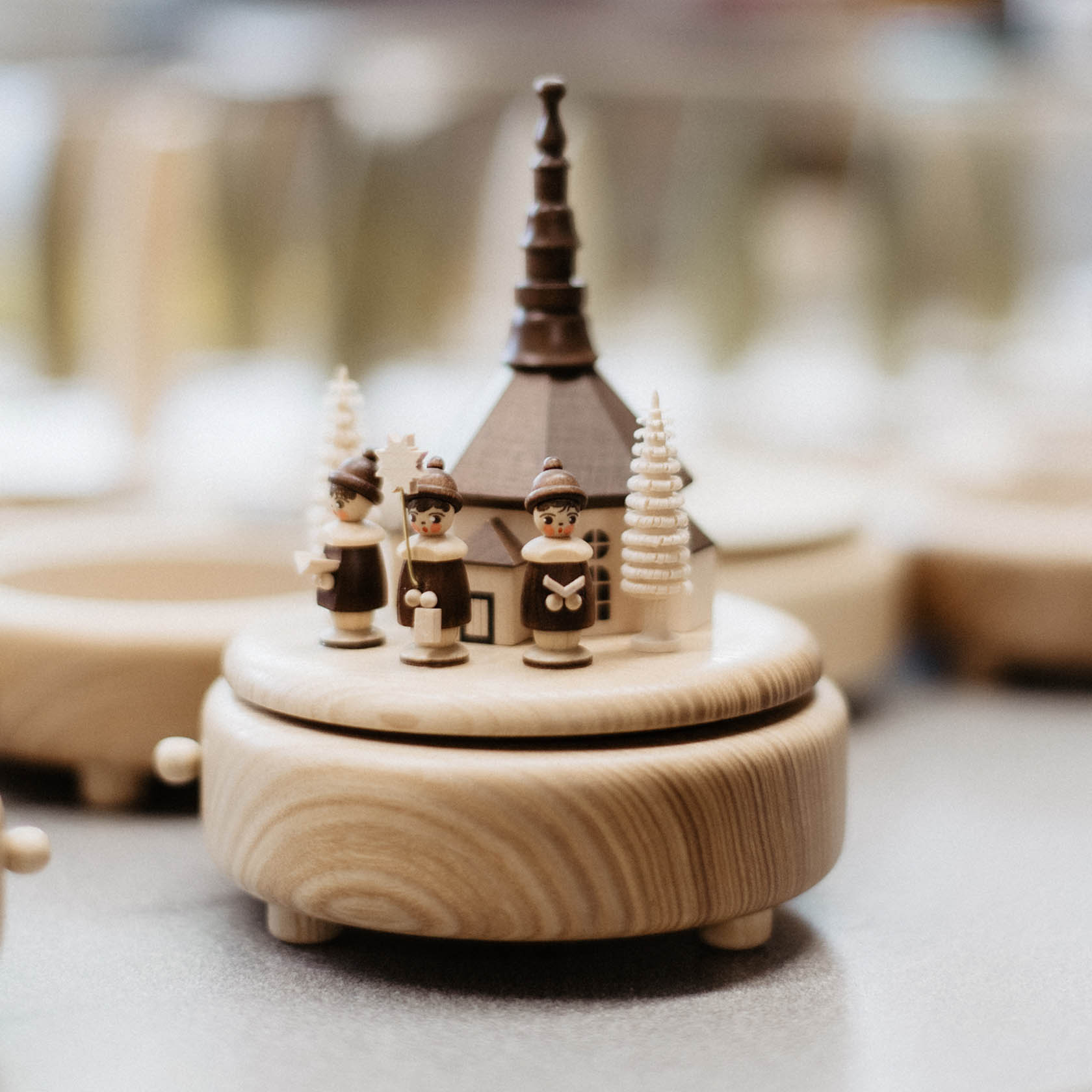 Handgefertigte Spieldose mit Seiffener Kirche und drei braun gekleideten Kurrende-Figuren. Die Figuren halten Notenblätter in den Händen.