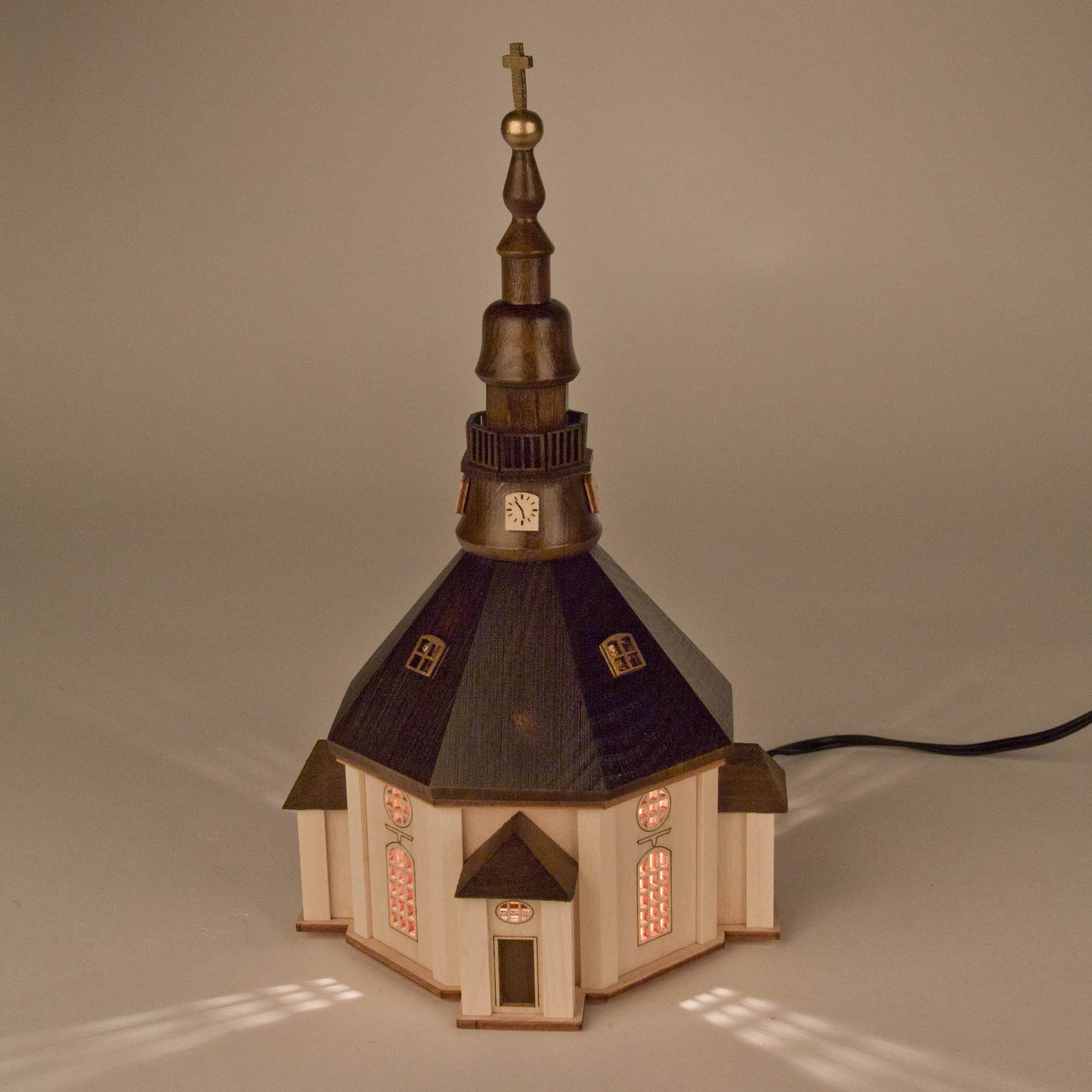 Illuminated wooden model of the Seiffen Church with a tall steeple and glowing windows, displaying intricate craftsmanship.