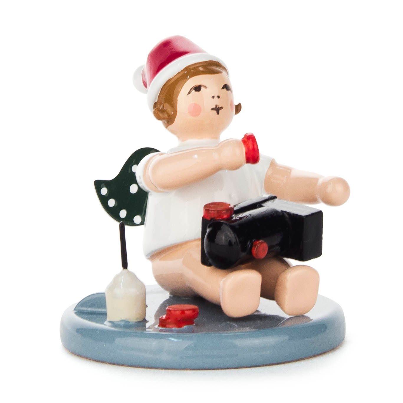 A sitting angel figurine with a red and white cap, holding a small black toy train and a red glue pot, on a blue base. im Dregeno Online Shop günstig kaufen