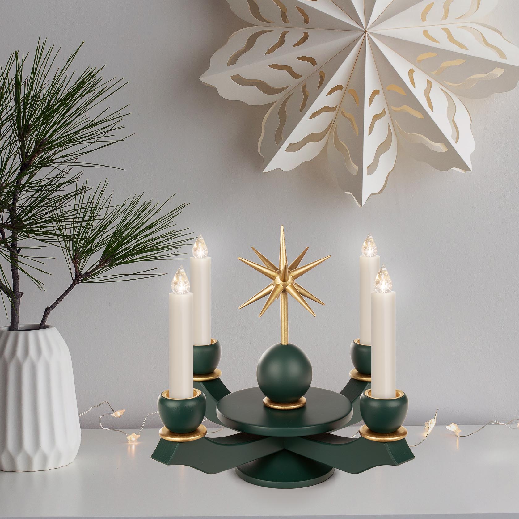 Grüner Adventsleuchter mit fünf Kerzenhaltern und goldenem Stern in der Mitte, dekoriert mit weißen Wachskerzen.