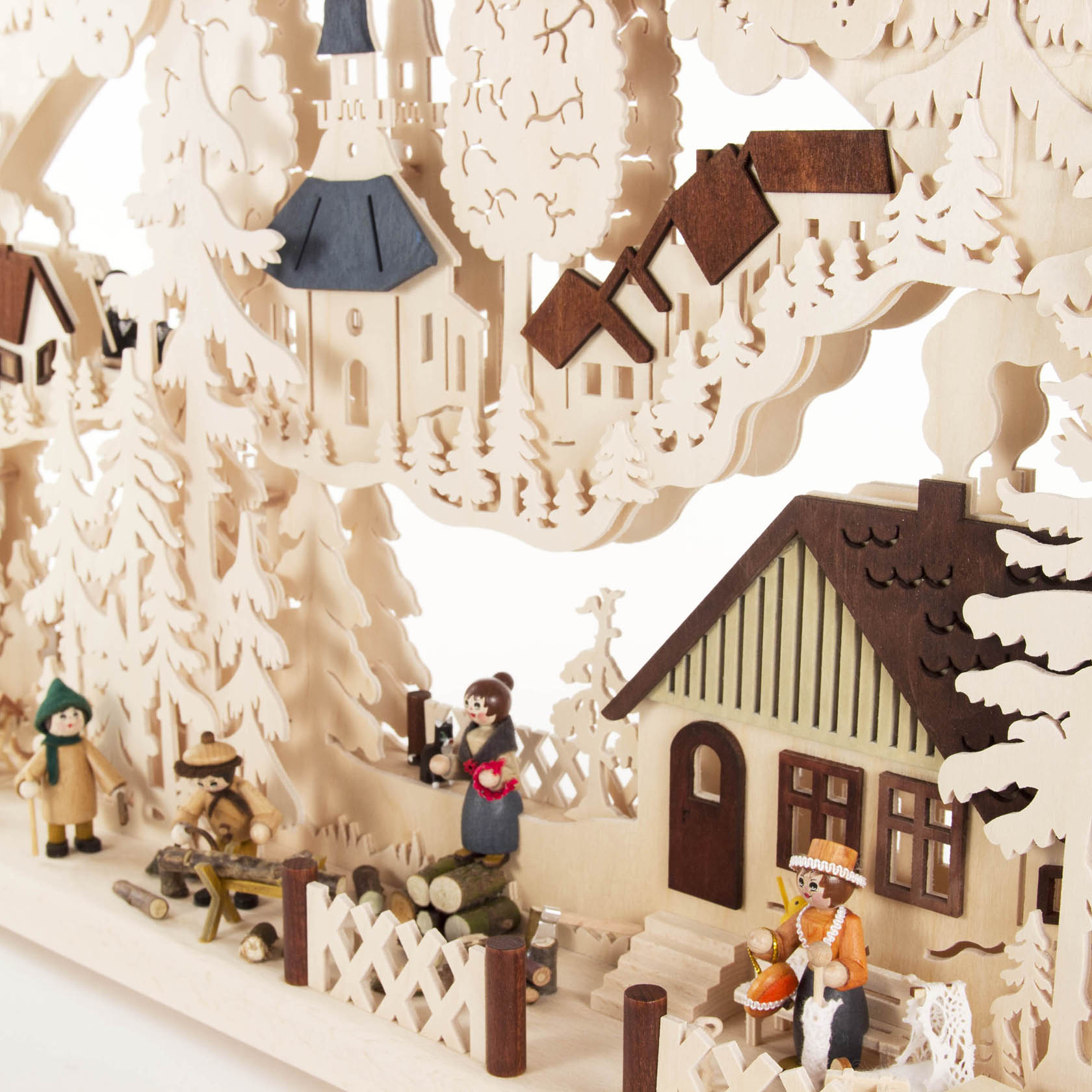 Wooden arch featuring a village scene with a church, trees, and houses. Figurines depict people, including a man with an accordion and a boy with a sled.