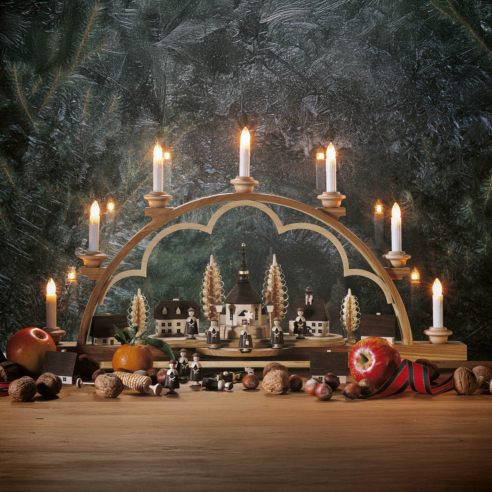 An illuminated wooden arch (Schwibbogen) featuring a miniature Seiffener village with Kurrende figures, surrounded by lit candles.