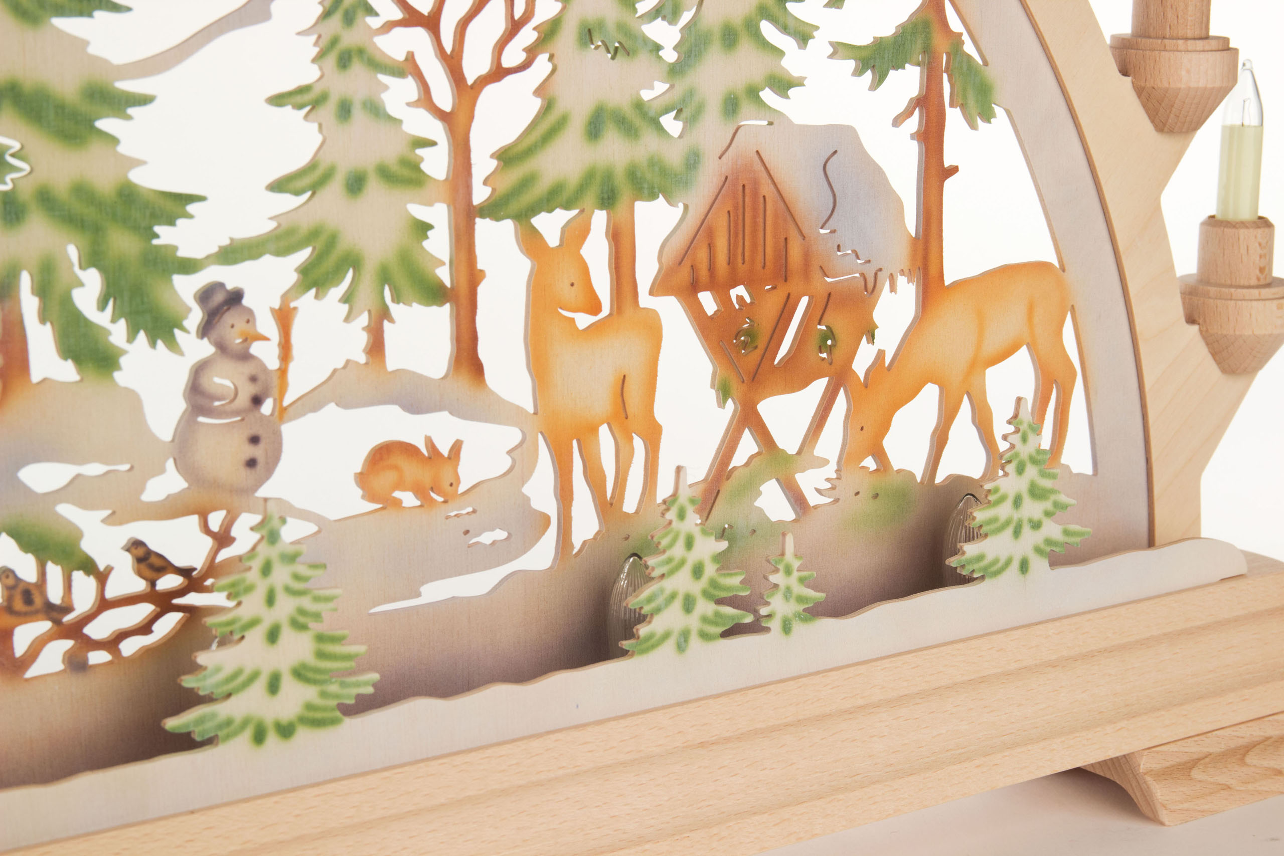 Ein Schwibbogen aus Holz mit farbiger elektrischer Beleuchtung zeigt ein Waldmotiv mit zwei Rehen, einem Futterhaus, einem Schneemann und einem Hasen.