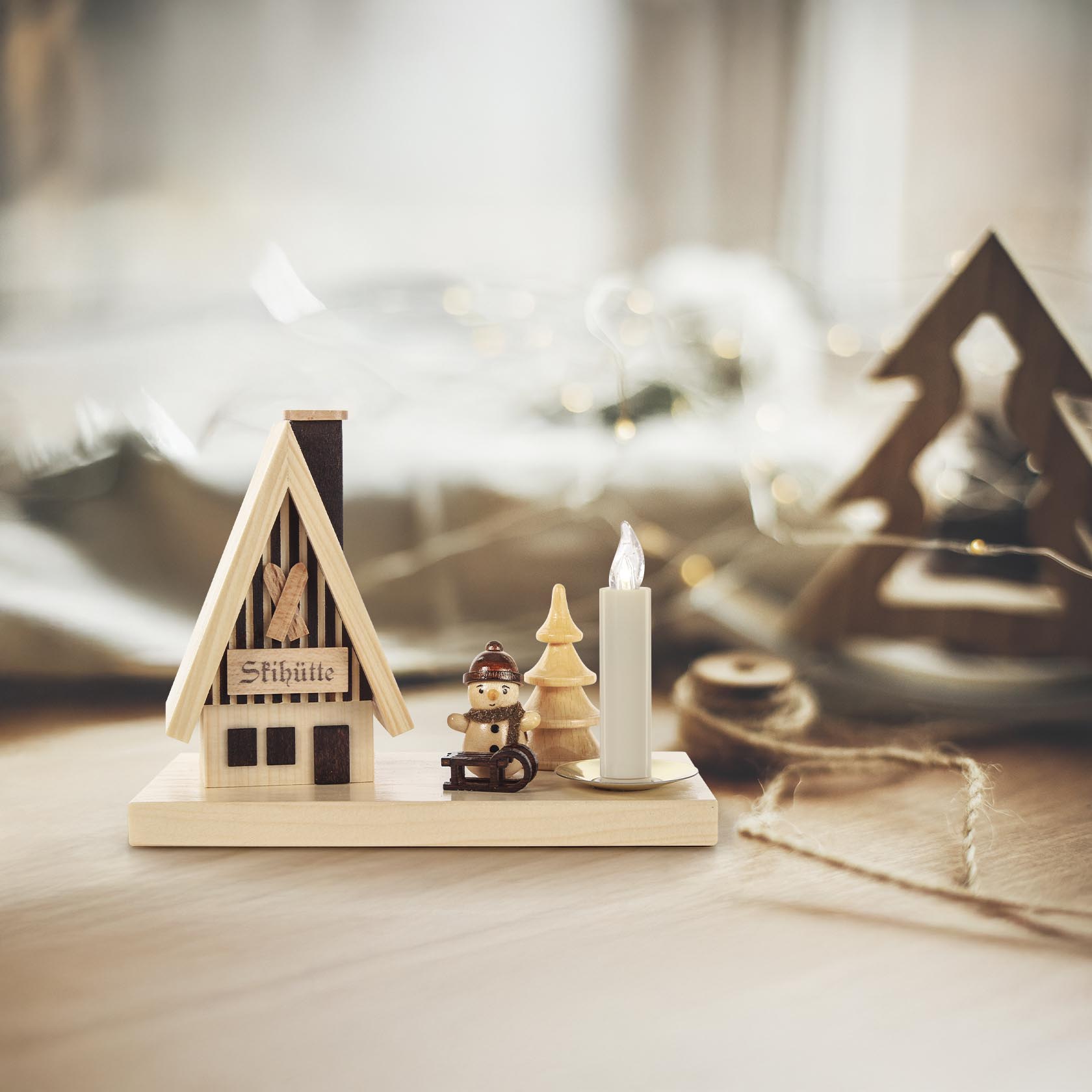 Miniatur Holzskulptur eines Räucherhauses mit Beschriftung 'Skihütte', ein kleiner Schneemann mit Mütze auf einem Schlitten und ein Kerzenhalter aus Holz.