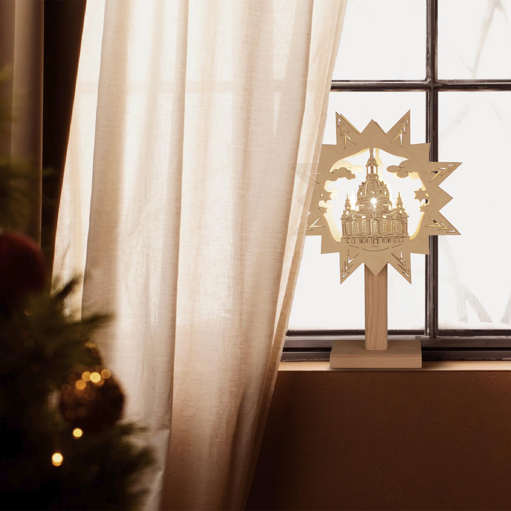 Fensterbild mit der Silhouette der Frauenkirche auf einem Holzsockel, beleuchtet durch elektrische Lichter, steht auf einer Fensterbank neben einem Vorhang.