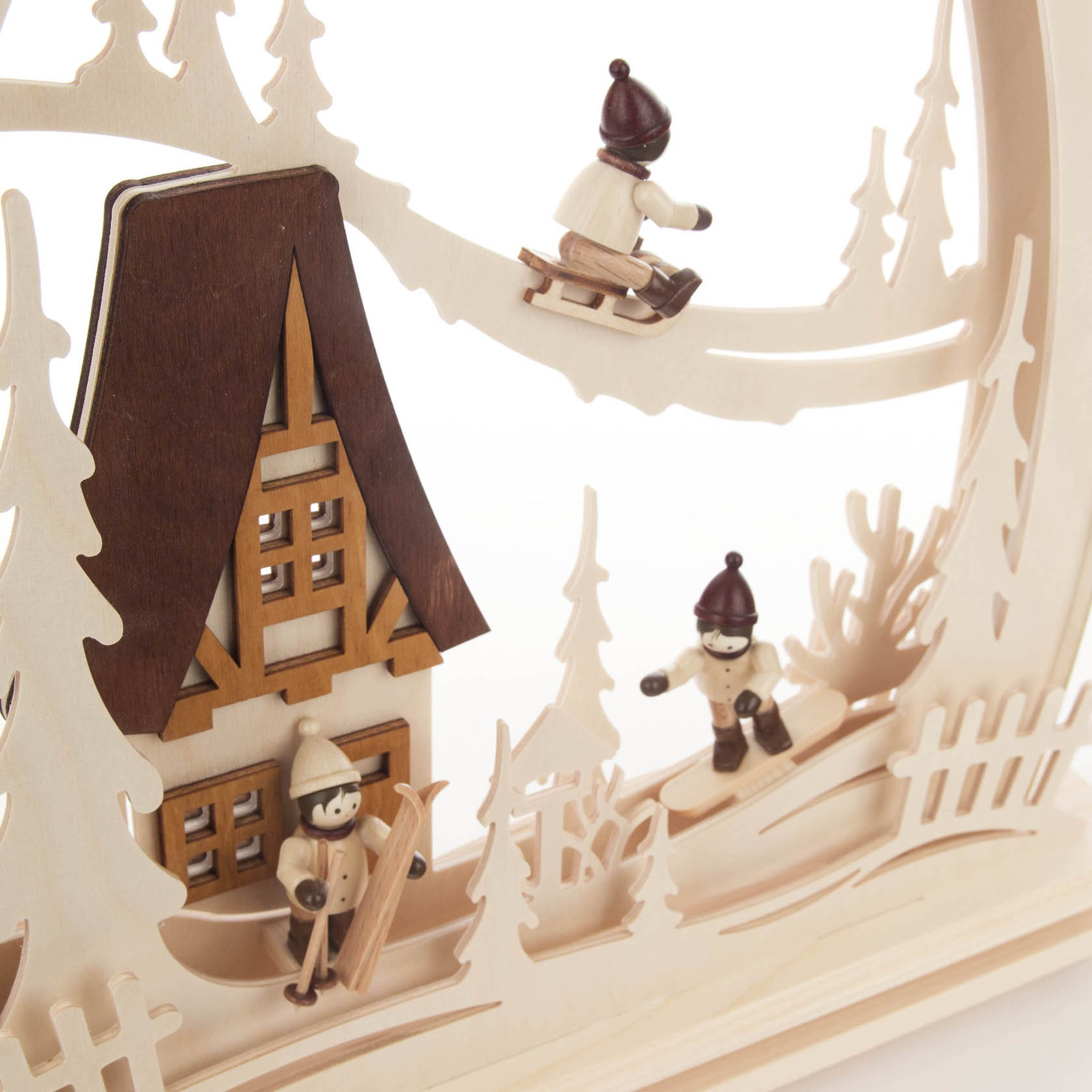 Holzbogen mit zwei Holzfiguren in winterlicher Kleidung, die auf Skiern und einem Schlitten sind, vor einem Haus und Bäumen, mit LED-Beleuchtung.