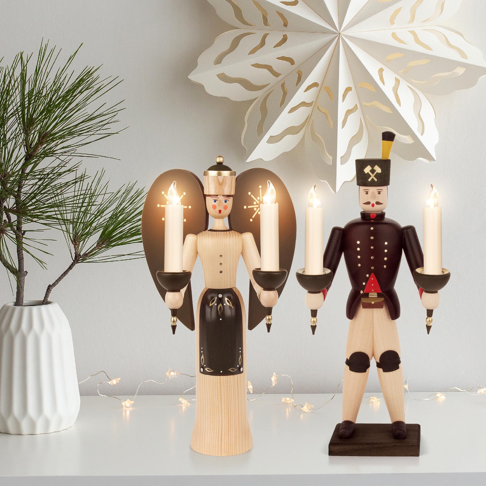 Zwei hölzerne Figuren mit Kerzenhaltern: Links ein Engel in naturfarbenem Gewand und schwarzen Flügeln, rechts ein Bergmann in traditioneller Bergmannstracht.