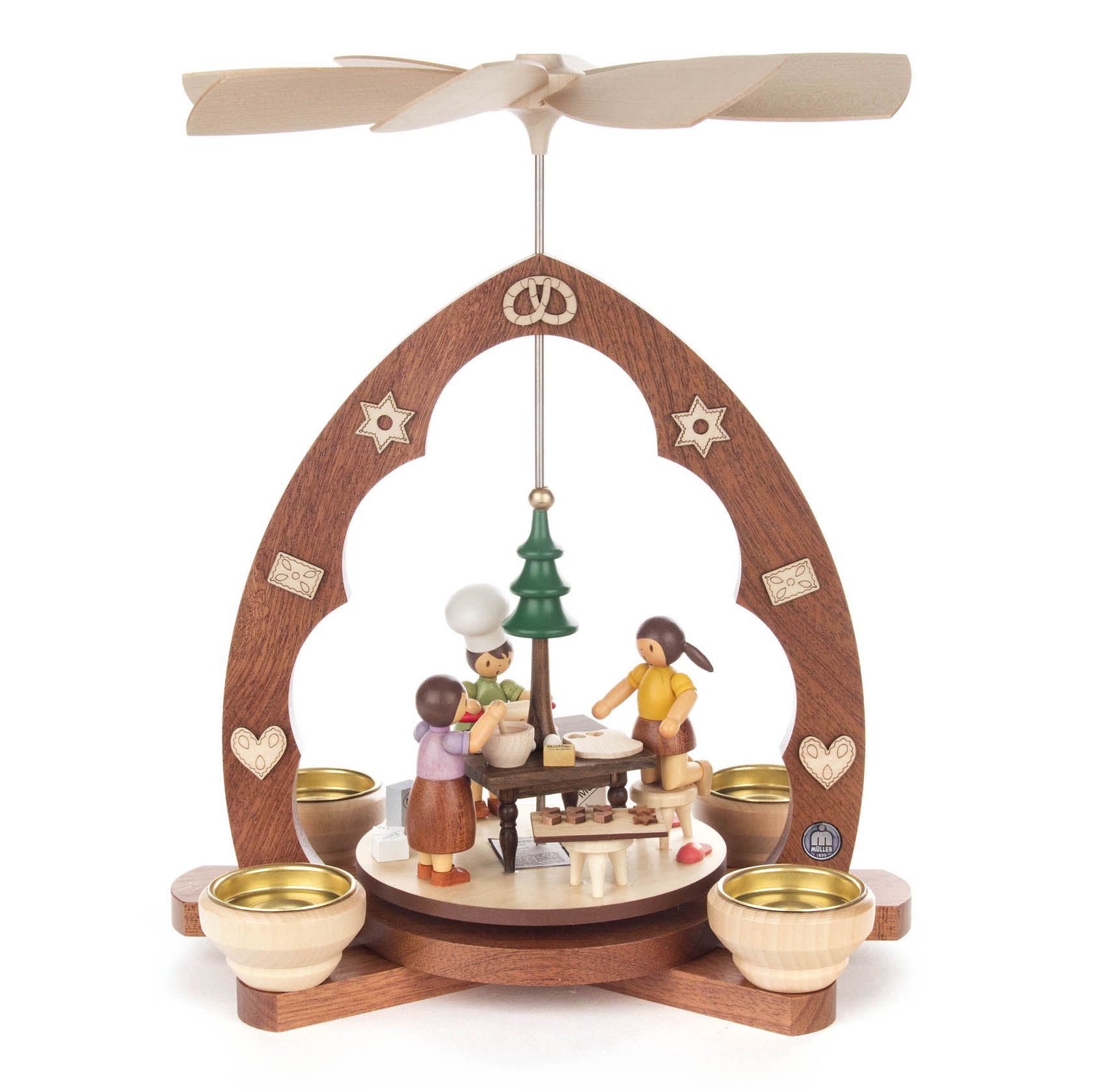 Eine Weihnachtspyramide mit drei Holzfiguren in einer Bäckerei-Szene. Zwei Frauen und ein Mann stehen um einen Tisch mit einem Baum darauf.