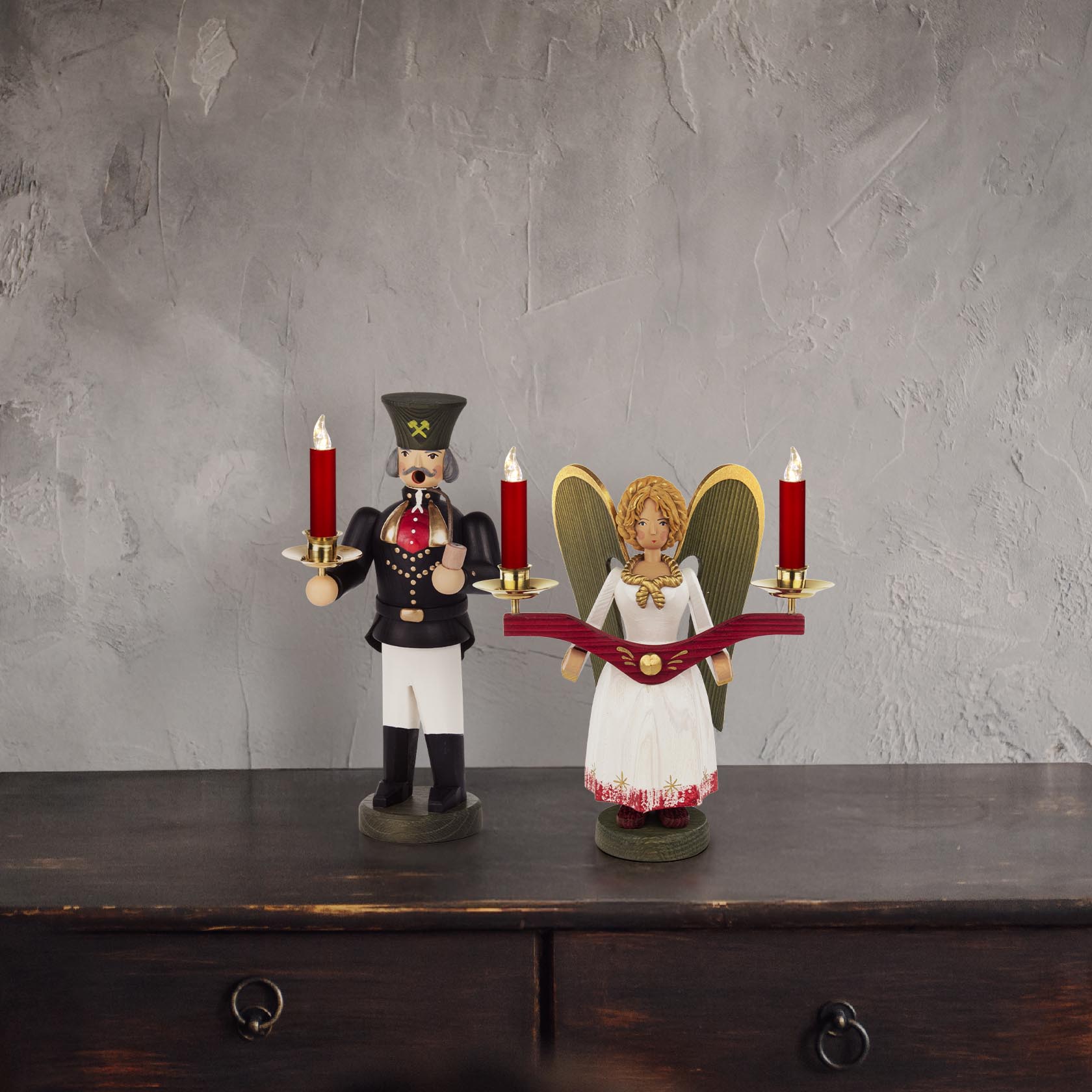 Ein Lichterengel und ein Bergmann-Figurenpaar. Der Engel hält zwei Kerzen, trägt ein weißes Kleid und goldene Flügel. Der Bergmann trägt eine Uniform und einen Hut.