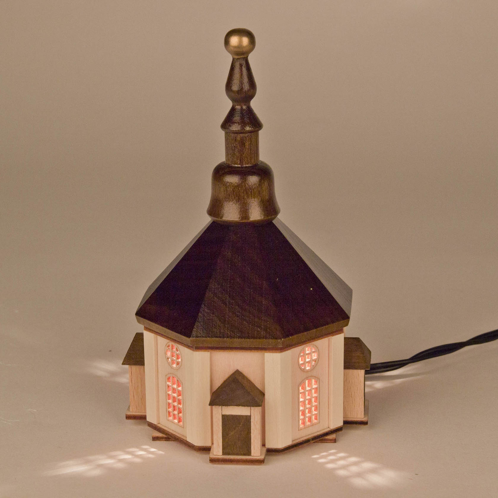 A small, illuminated Seiffen church replica featuring a hexagonal base, wooden windows, and a tall, decorative steeple.