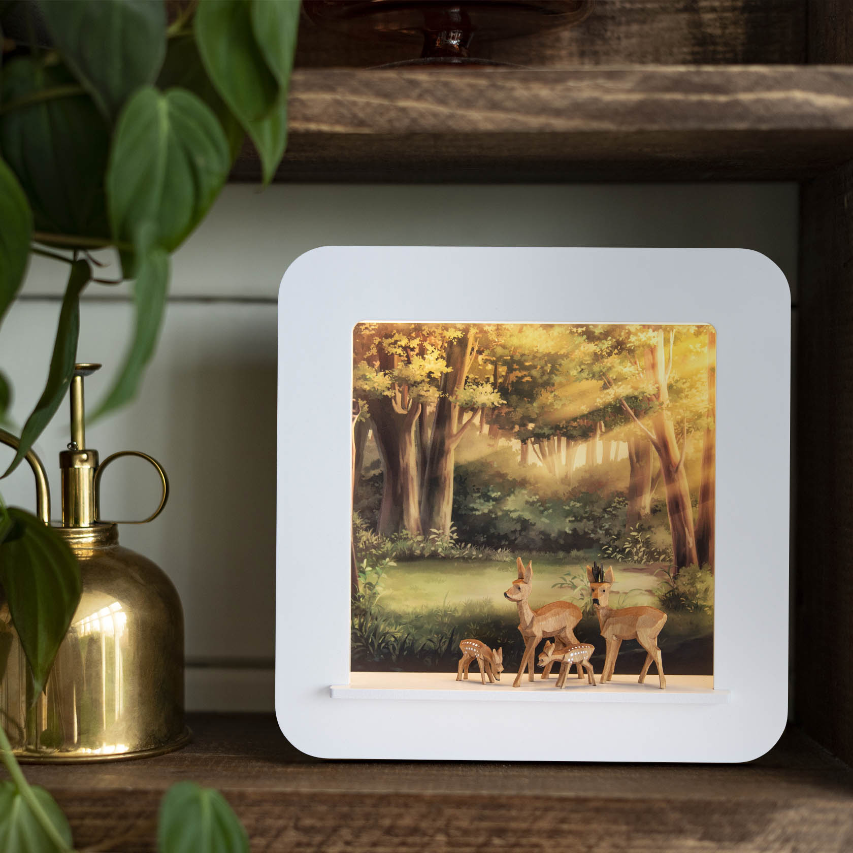 A 3D illuminated frame depicting three deer in a forest setting. The deer stand gracefully against a backdrop of sunlit trees with LED lighting enhancing the scene.