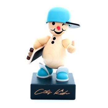 A wooden figurine of a playful snowman wearing a blue baseball cap and shoes, holding a skateboard and winking, standing on a black base with 'City Kids' signature.