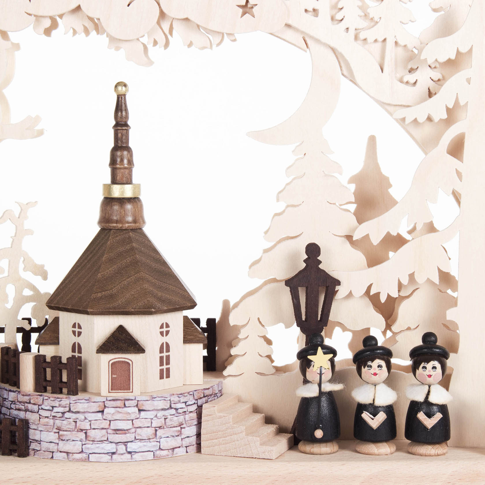 Ein Schwibbogen zeigt eine kleine Dorfkirche mit einem braunen Dach und Holzzaun. Drei Holzmännchen in traditioneller Kleidung stehen daneben.