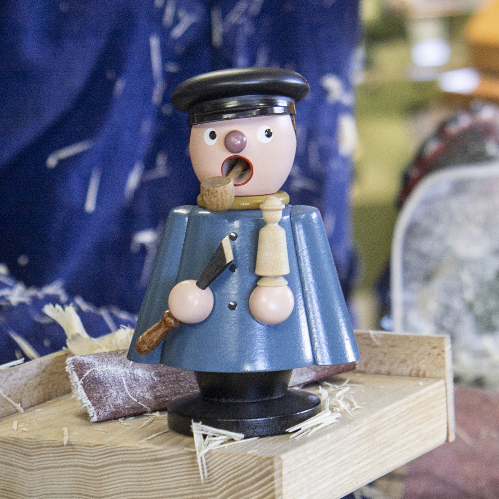 A traditional German incense smoker figurine depicting a craftsman with a pipe, wearing a blue coat and a black hat, holding a tool.