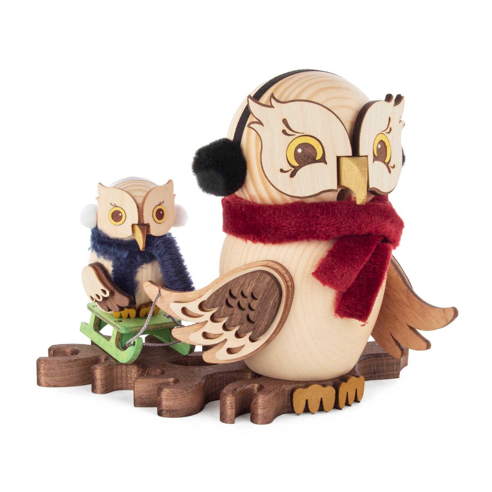 A wooden smoking owl figurine wearing earmuffs and a red scarf, with a smaller owl on a sled behind it, both crafted with intricate details.