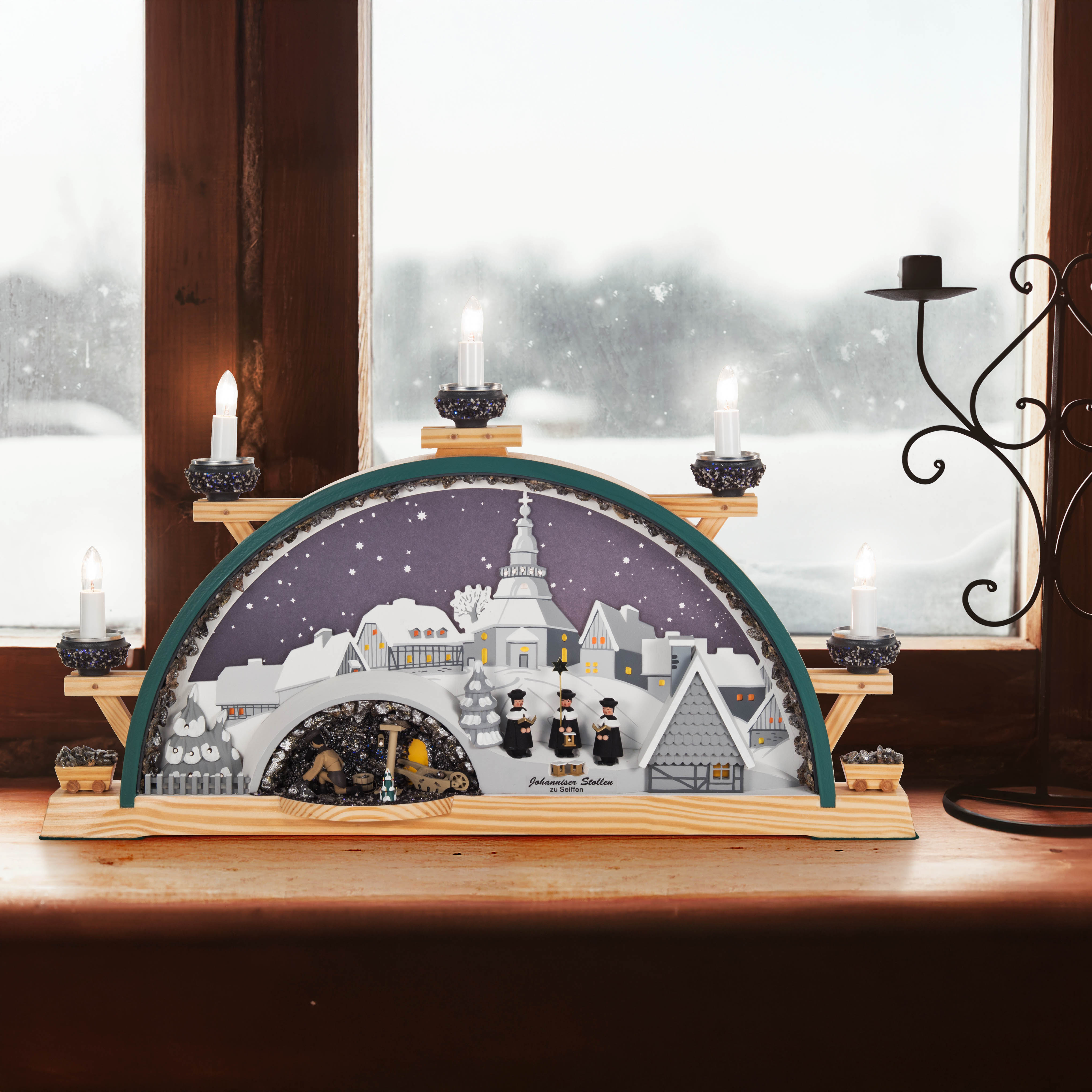 Illuminated Schwibbogen featuring Seiffen village, a miner's band, and a mine scene, placed on a window sill with lit candles.
