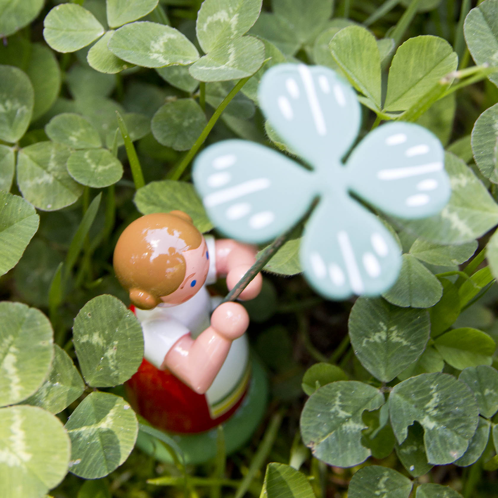 Playmobil-Figur eines Mädchens hält einen großen weißen Glücksklee mit vier Blättern, umgeben von echtem Kleeblatt.