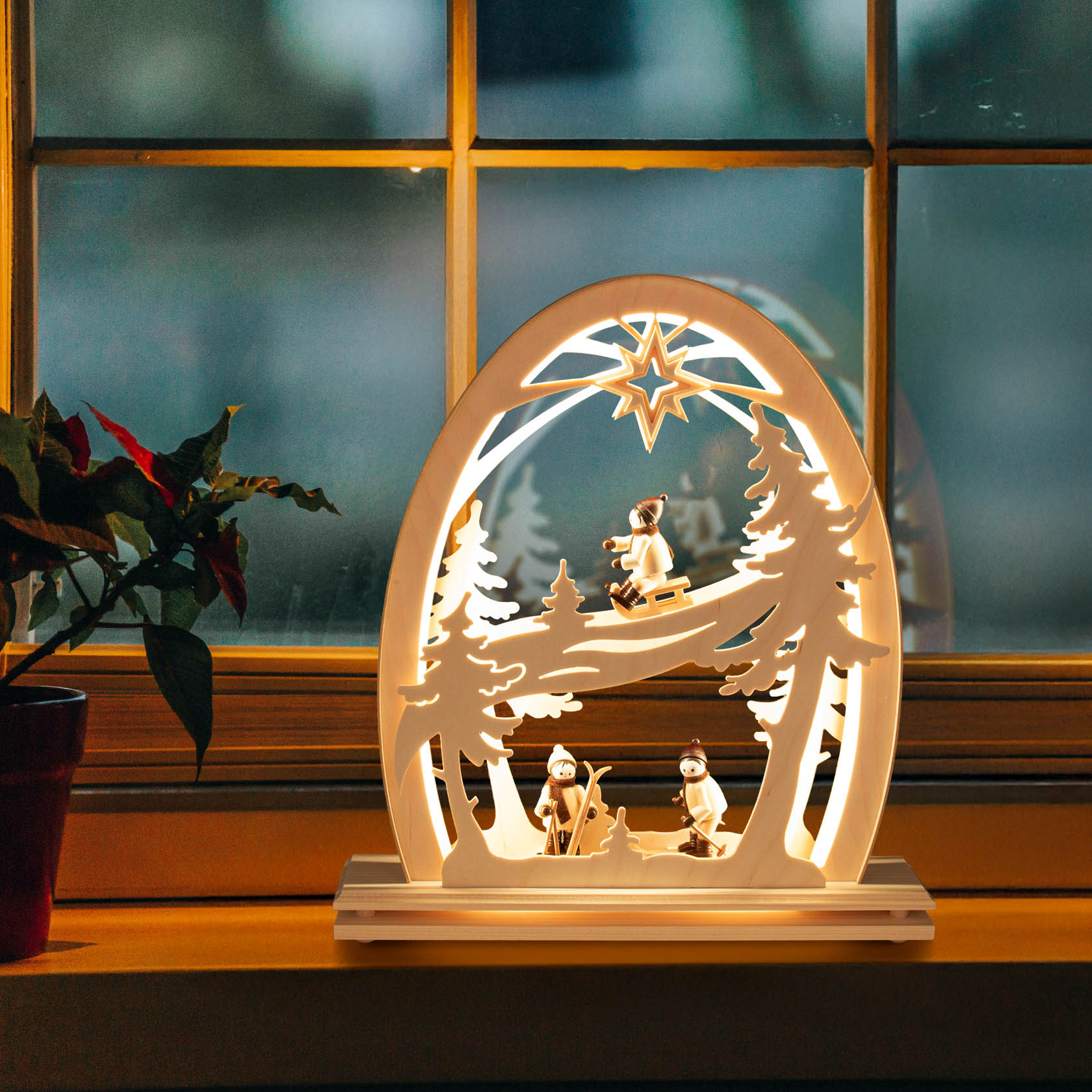 Electric LED Erzgebirge arch with illuminated winter sports figures, depicting skiers under a star atop the arch, set on a window sill.