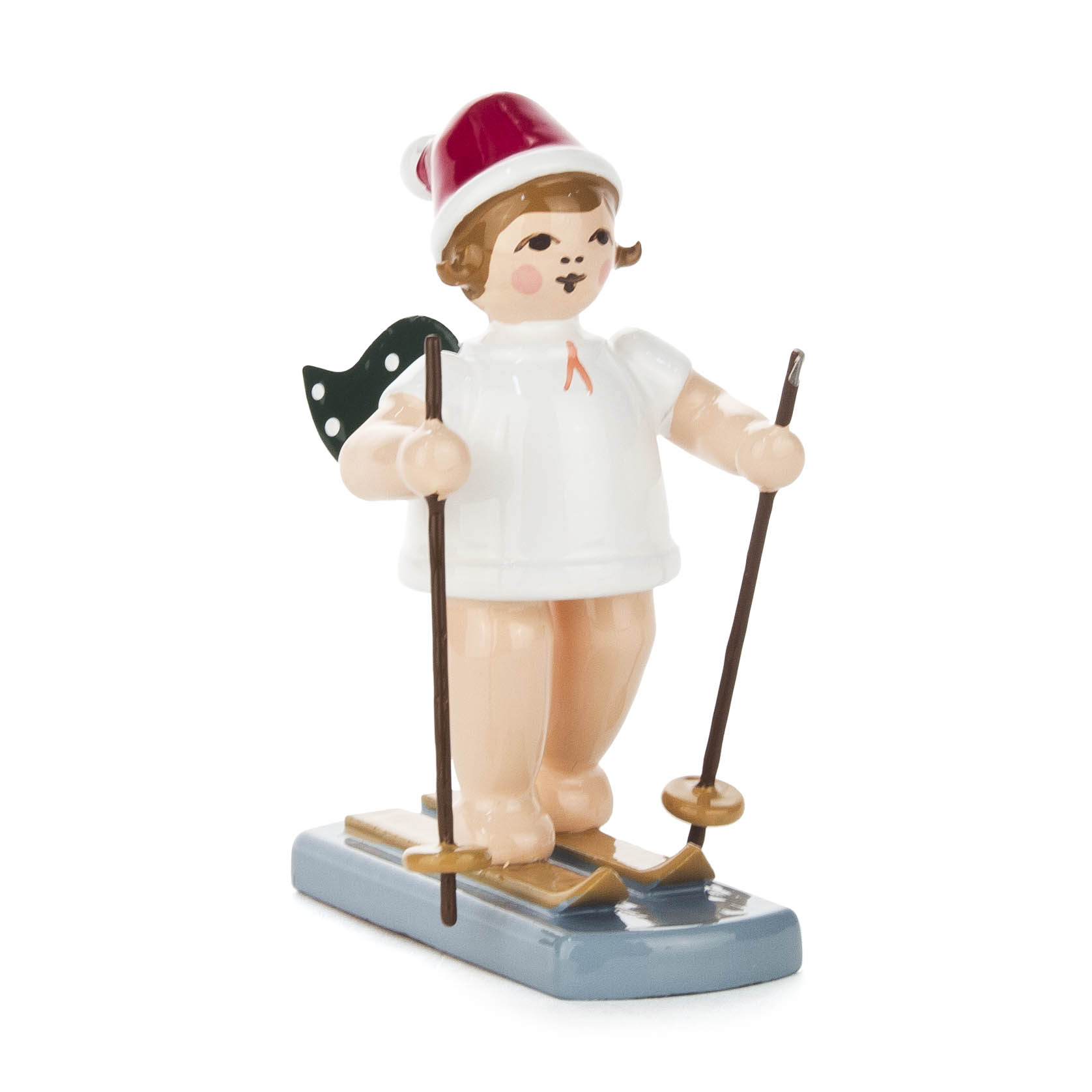 A wooden figurine of an angel skier with rosy cheeks, wearing a red hat and holding ski poles, standing on a blue base. im Dregeno Online Shop günstig kaufen