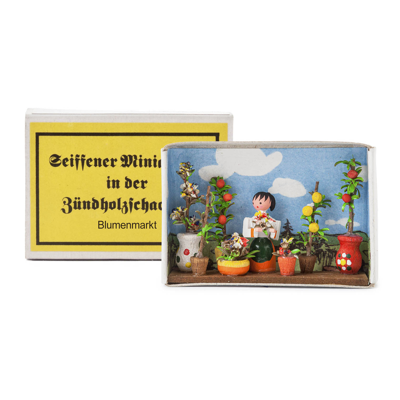 A matchbox shows a small diorama of a flower market with a smiling child figure holding flowers among various potted plants. im Dregeno Online Shop günstig kaufen