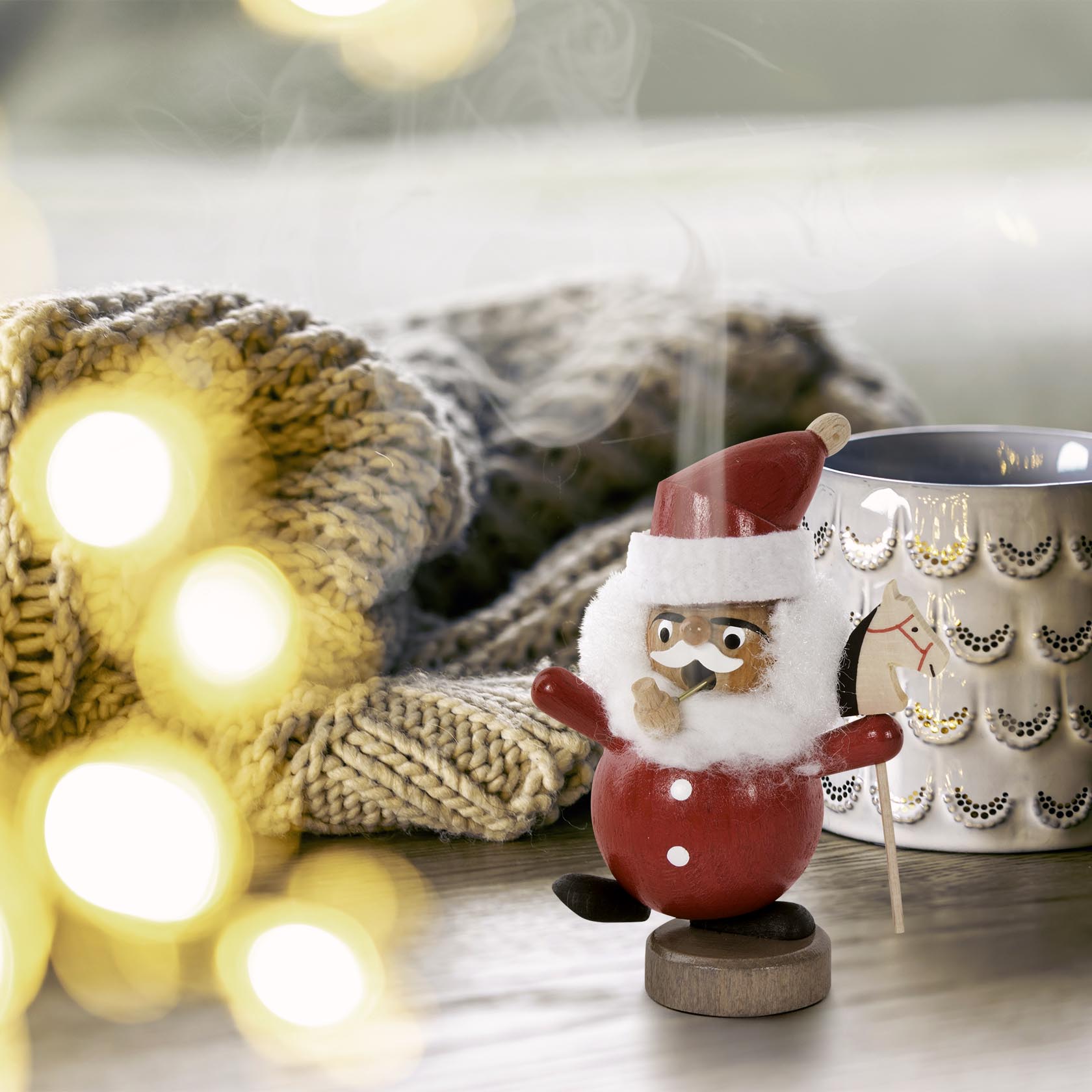 A miniature Santa Claus incense smoker figurine with a red outfit, smiling and holding a staff, standing on a wooden surface.