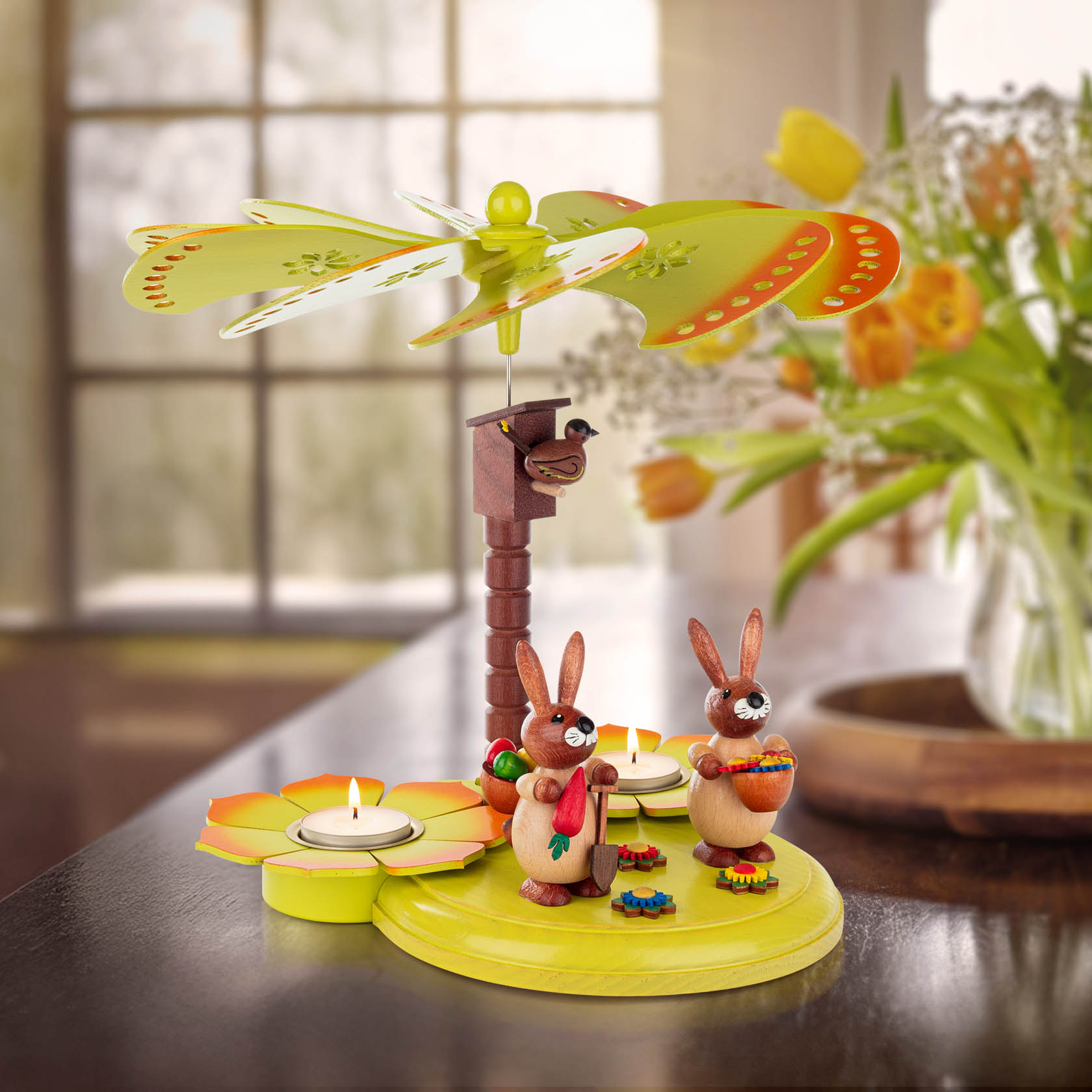 Colorful tea light pyramid with two wooden bunnies, one holding a carrot and the other a basket, under a decorative propeller.