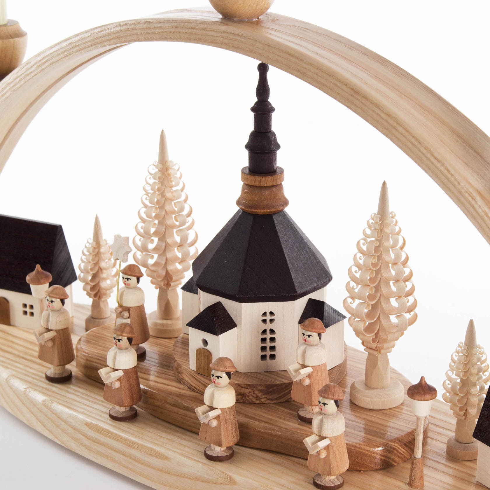 A wooden arch with a Seiffen village scene featuring a church, Kurrende singers, turned trees, and inside-lit buildings on a wooden base.