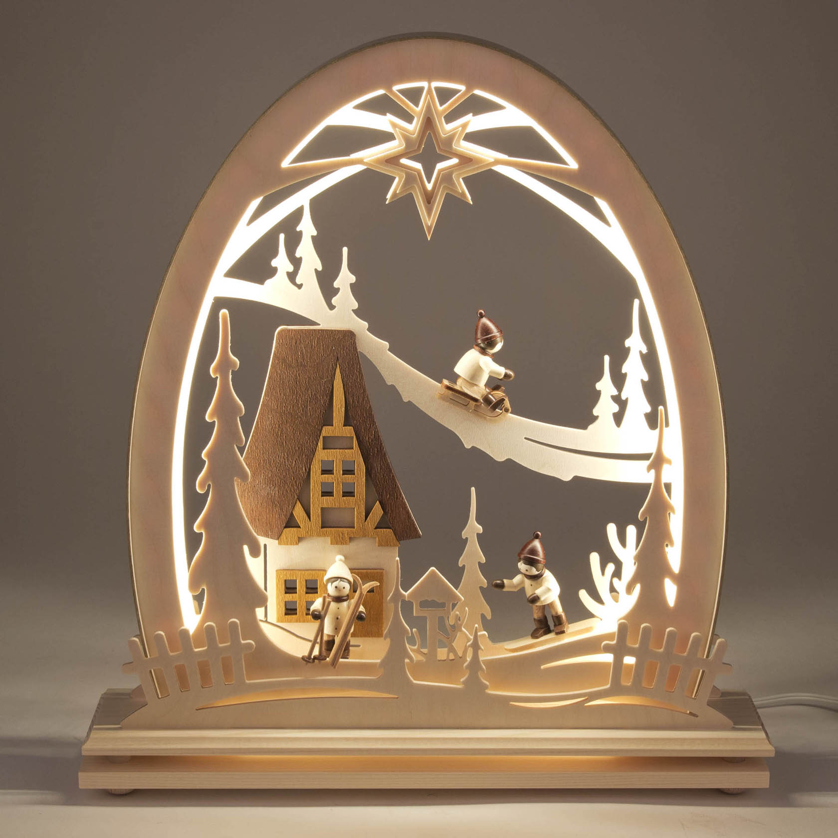 Erzgebirgsbogen mit zwei Winterkindern beim Schlittenfahren, einem beleuchteten Holzhaus und LED-Beleuchtung im Bogen.