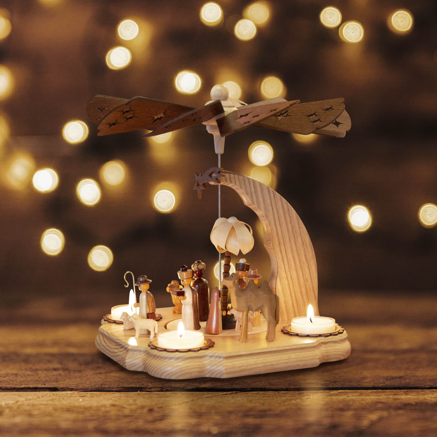 Holzpyramide mit der Darstellung von Christi Geburt, umgeben von Teelichthaltern. Eine Flügelradkonstruktion dreht sich durch die Wärme.