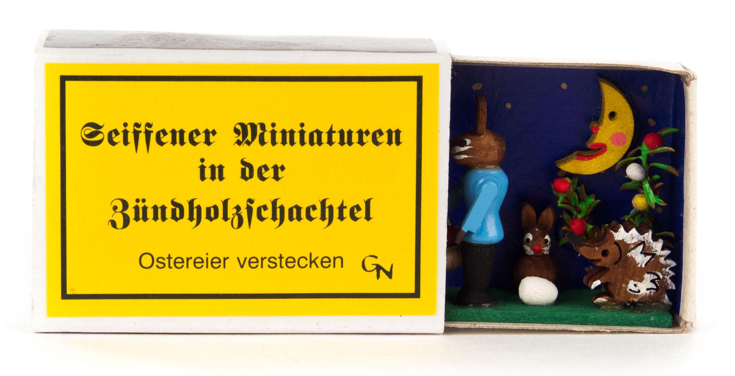 A tiny Easter scene inside a matchbox featuring hand-painted wooden figures: two rabbits, a hedgehog, a moon, and colorful Easter eggs.