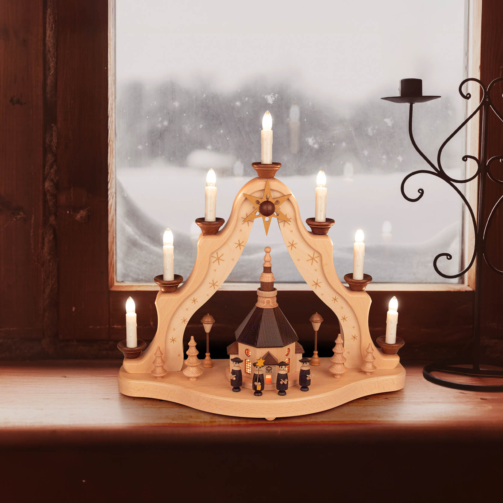 A wooden arch-shaped candle holder with electric lights on a window sill, featuring a small model of the Seiffener Kirche and decorative designs.