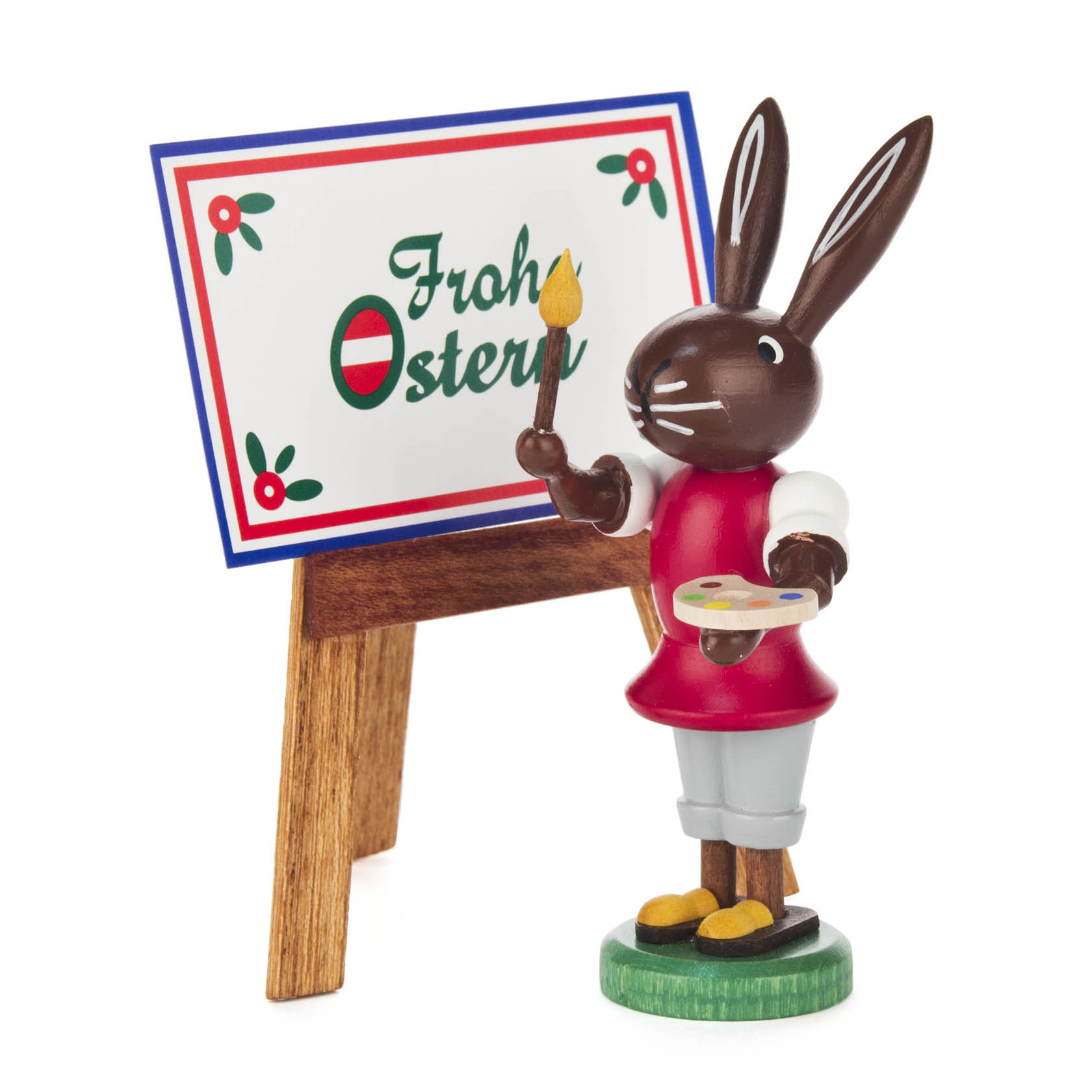 A wooden Easter bunny figurine stands holding a paintbrush and palette, next to an easel with 'Frohe Ostern' written on it.