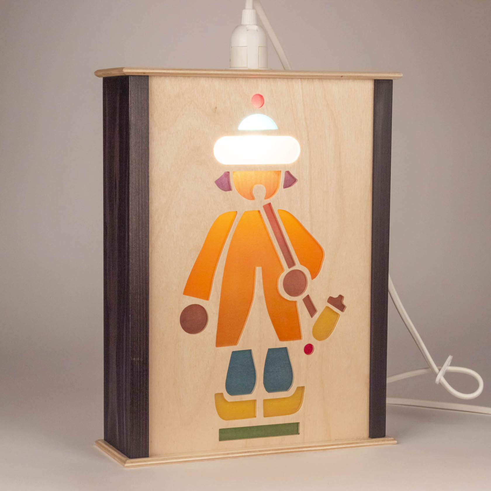 A wooden lantern with a silhouette of a rider, with colorful stained glass-like segments, and a corded electric light bulb on top.