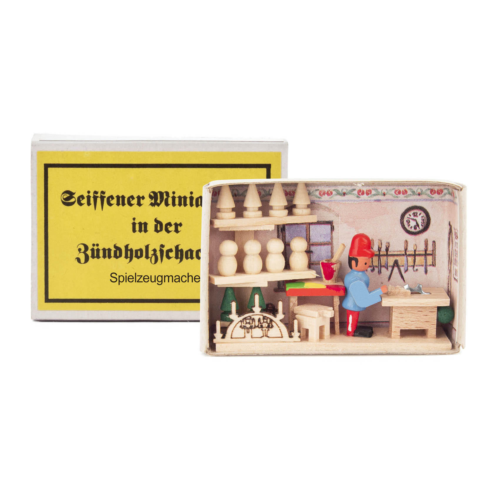 A small wooden figurine of a toy maker in a workshop inside an open matchbox. The workshop has tools, toy pieces, and shelves. im Dregeno Online Shop günstig kaufen