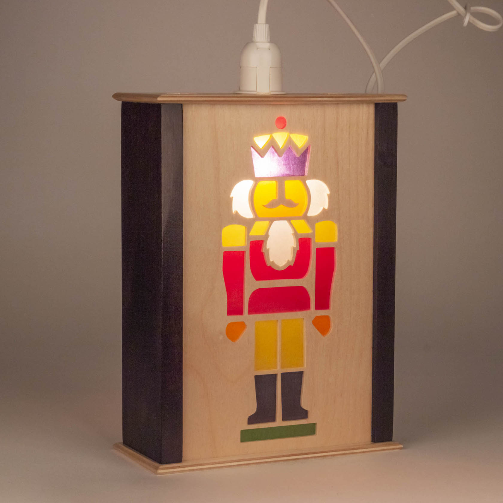 A small wooden window lamp featuring a brightly colored nutcracker figure with a crown, mustache, and uniform in red, yellow, and white.