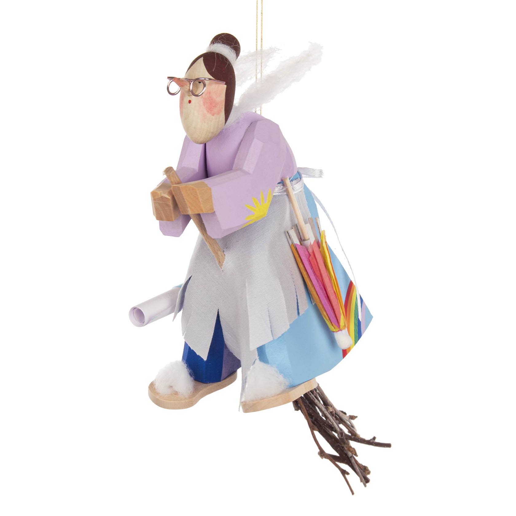 A wooden figurine of a witch wearing a purple coat and glasses, holding a stick and sitting on a broom. She carries paper rolls and a colorful umbrella in her bag.