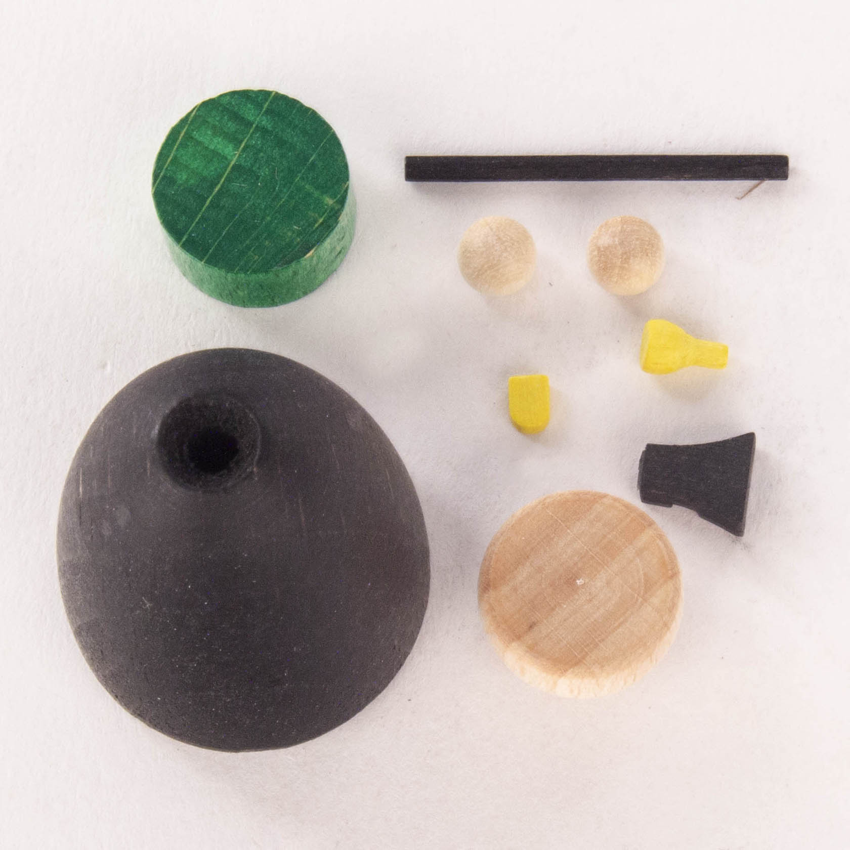Ein Bastelset mit Holzformen: ein schwarzer Kegel, ein grüner Zylinder, ein Holzkreis, ein schwarzer Stab, zwei Holzkugeln, zwei gelbe Teile und ein schwarzes Stück.
