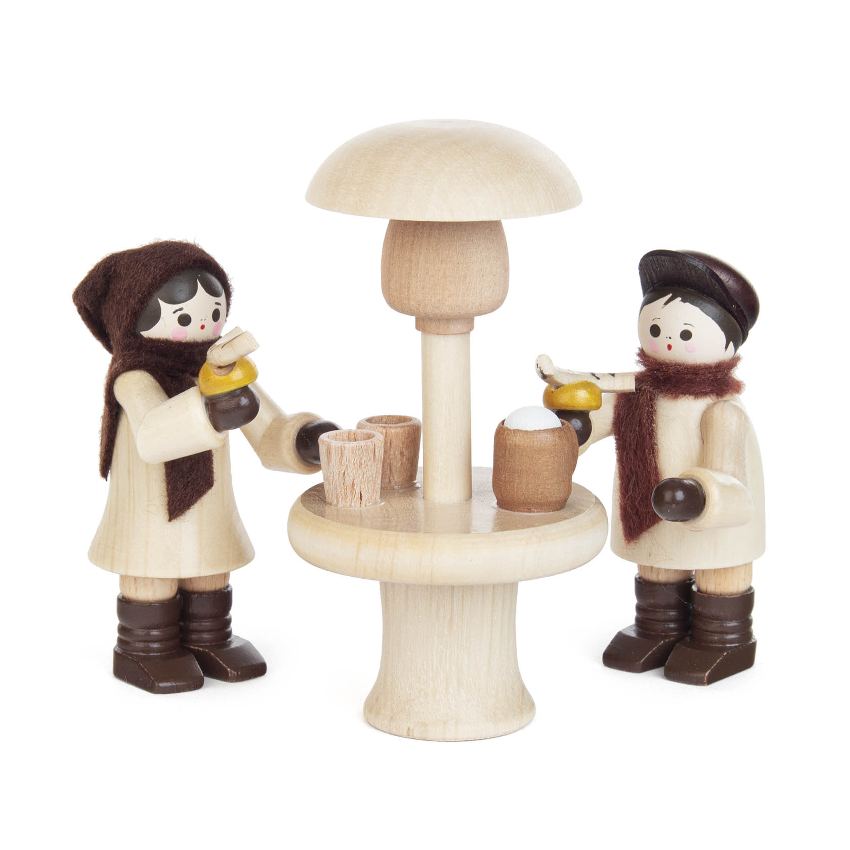 Zwei Holzfiguren in Winterkleidung stehen an einem hölzernen Stehtisch mit integriertem Heizstrahler, halten Tassen und eine Teekanne.