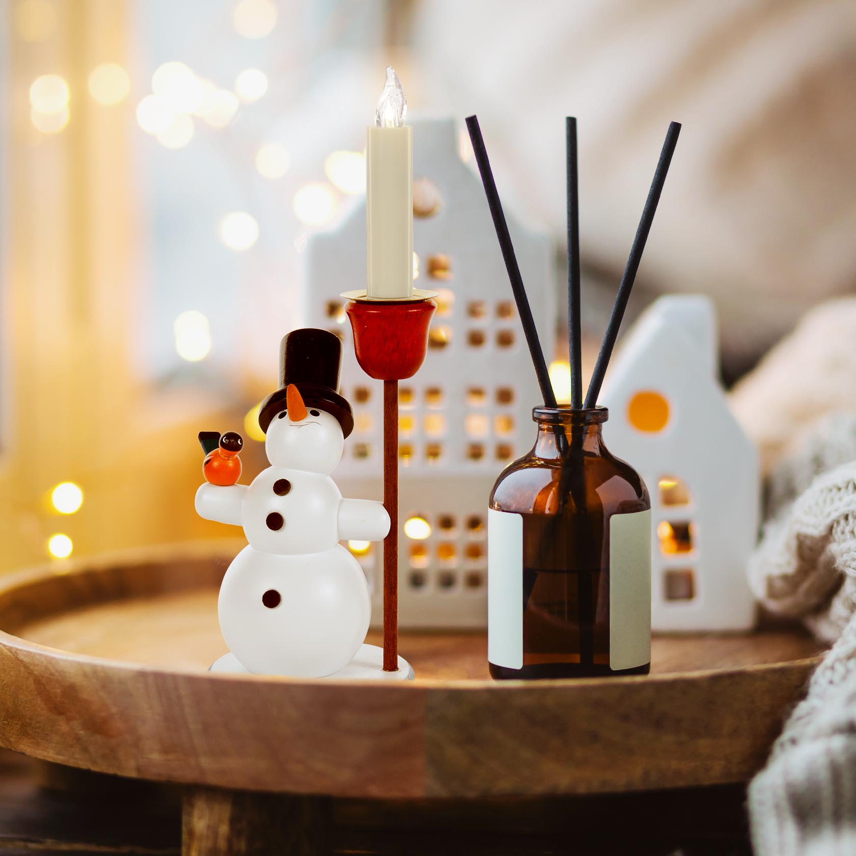 Glass snowman with black top hat holds a red candle holder for 14mm candles, placed beside a brown bottle with black sticks and miniature house decor.