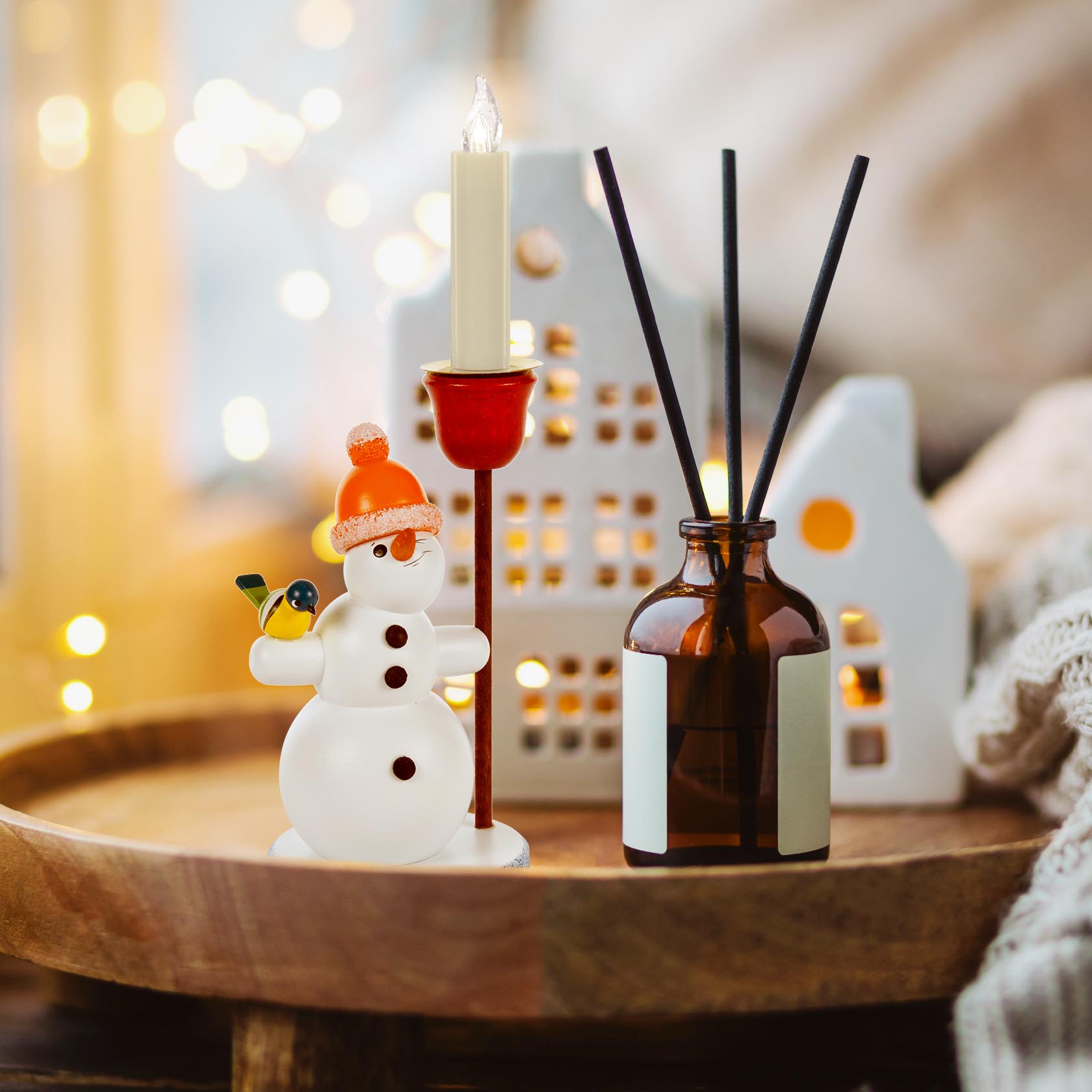 Glass snowman with an orange pom-pom hat holding a candle holder for a 14mm candle, with a candle lit on a wooden tray.