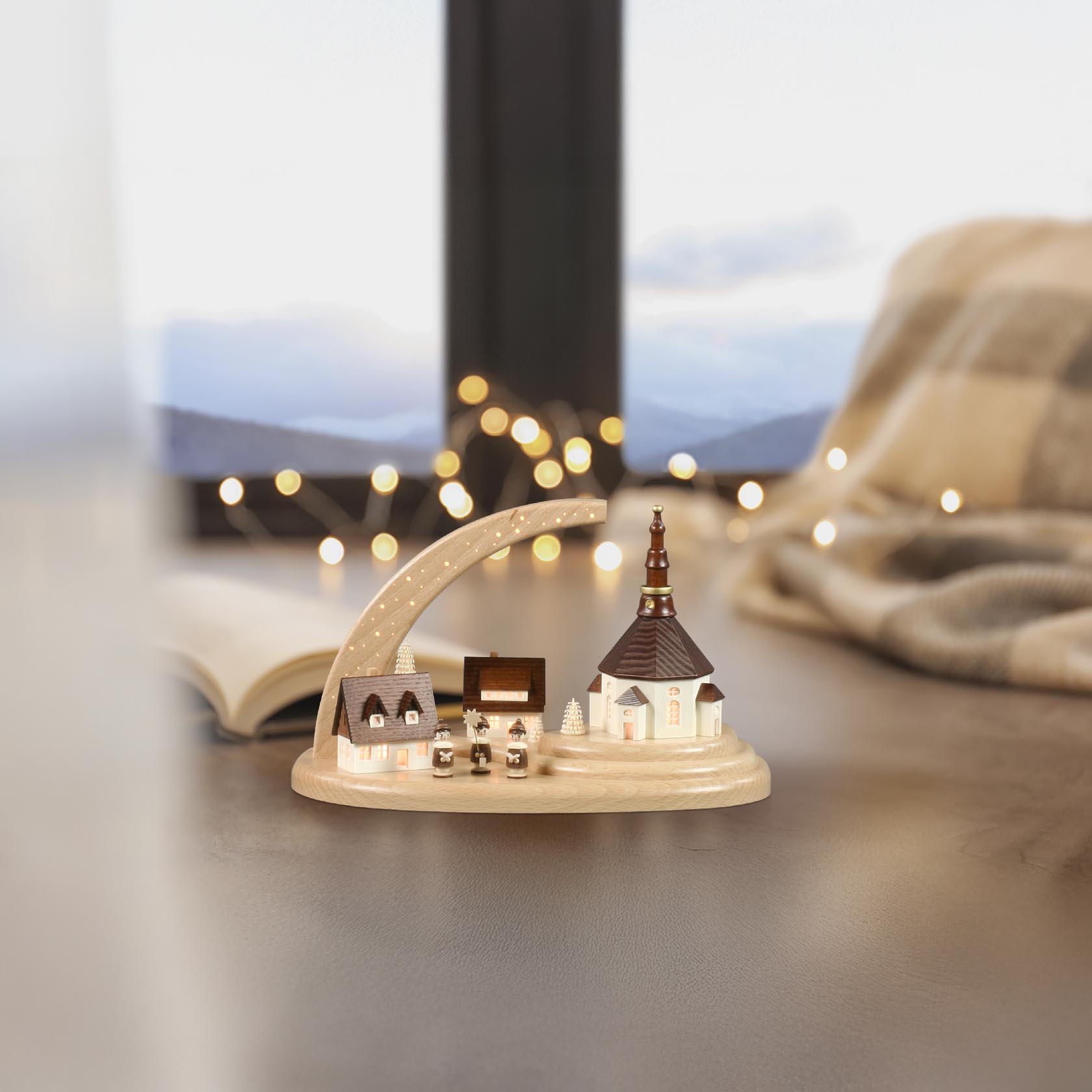 A handcrafted Seiffen village with a church, small houses, and figurines under a starry arch, all illuminated with electric interior lights.