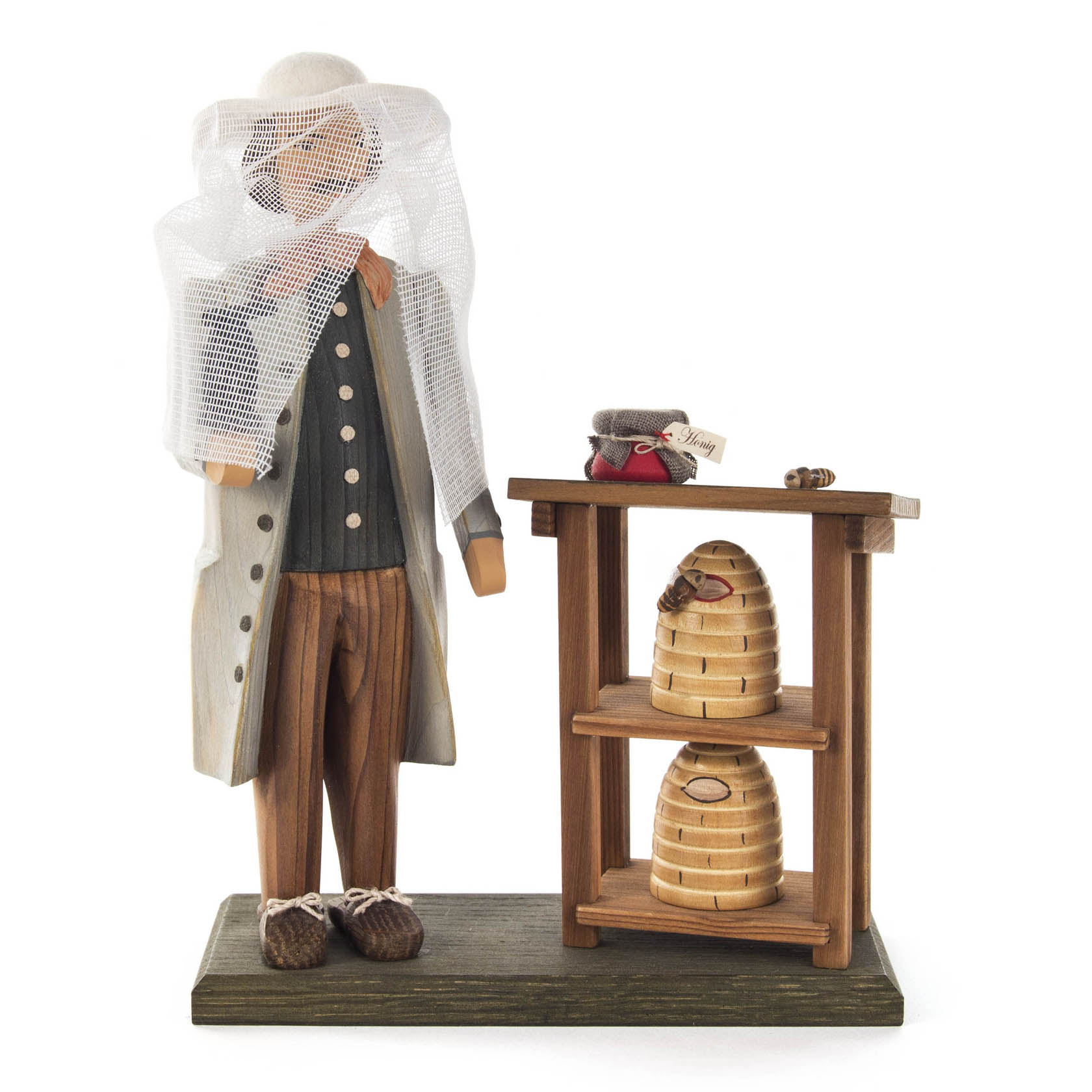 Holzfigur eines Imkers mit Schutzkleidung steht neben einem Regal mit zwei Bienenkörben.