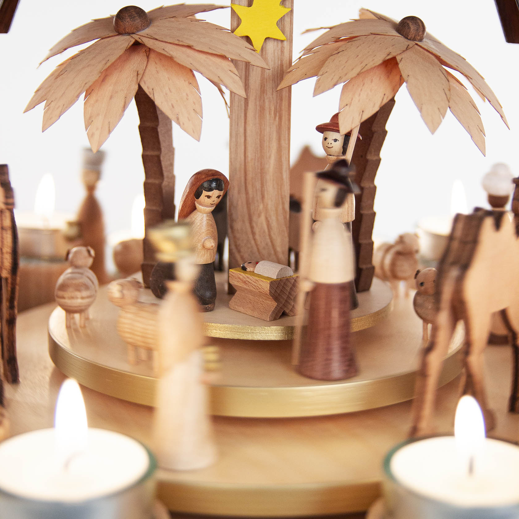 Wooden nativity scene with figures of Mary, Joseph, Baby Jesus, palm trees, and candles on a tiered pyramid structure.