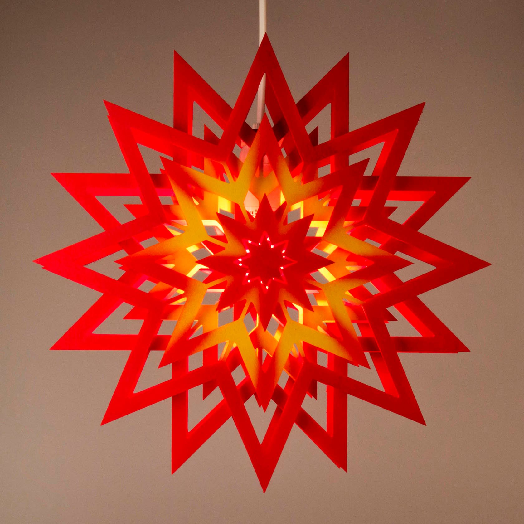 Leuchtender roter Weihnachtsstern mit gelbem Mustern und elektrischer Beleuchtung, aufgehängt in einem Raum.